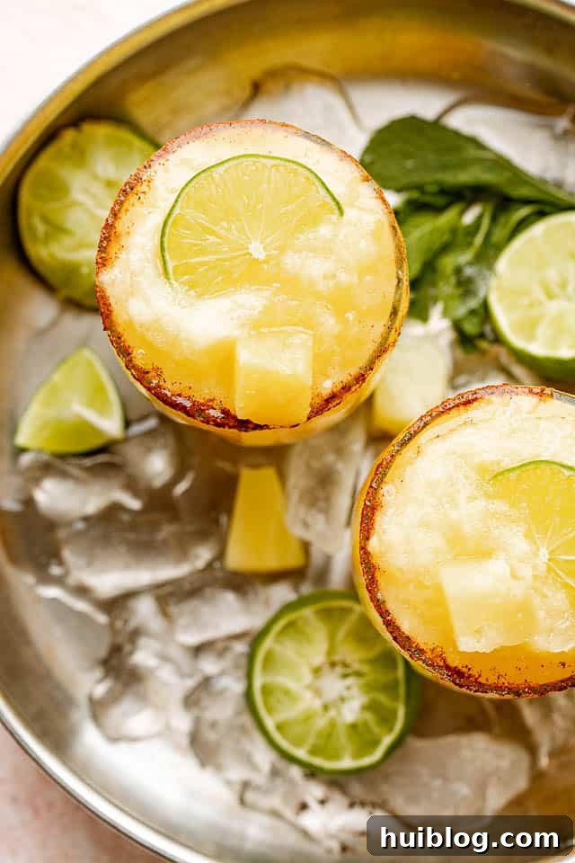 A delightful top-down view of two frozen pineapple margaritas, exquisitely garnished with fresh lime and pineapple, sitting pretty on a summer table.