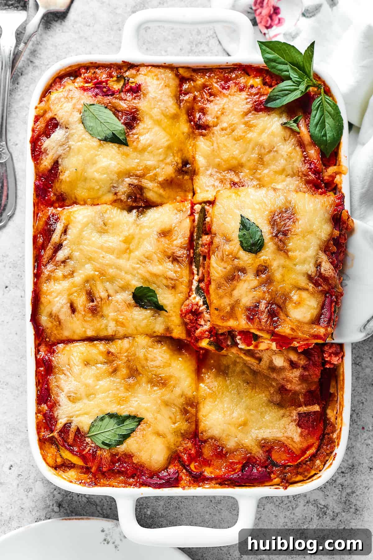 zucchini lasagna being lifted out of a white rectangular baking dish.