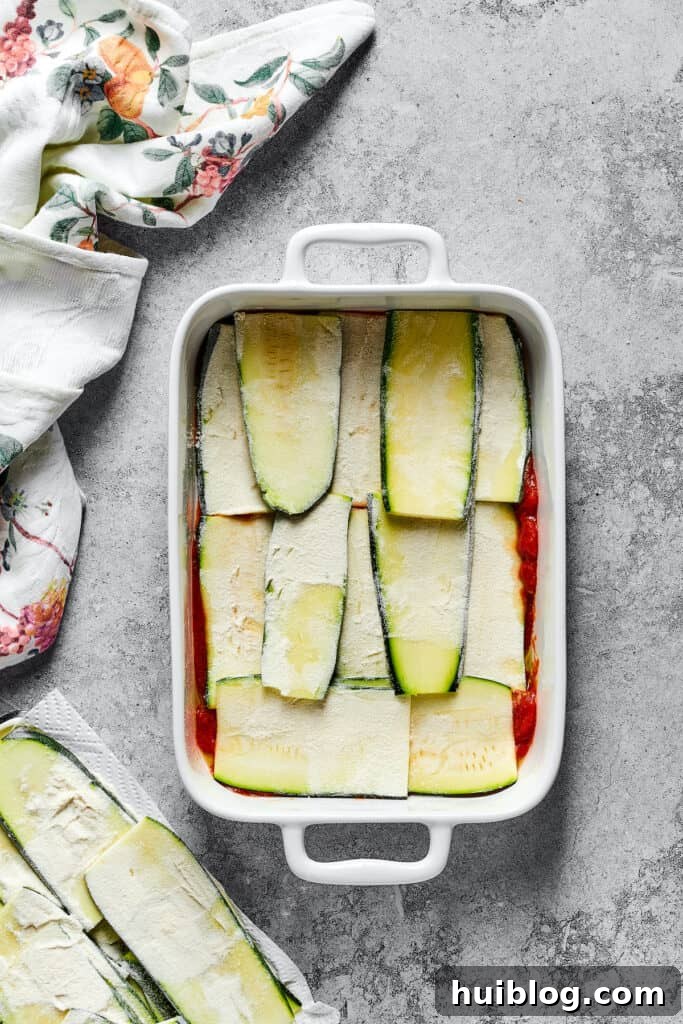 Strips of floured zucchini layered over a base of tomato sauce in a baking dish.