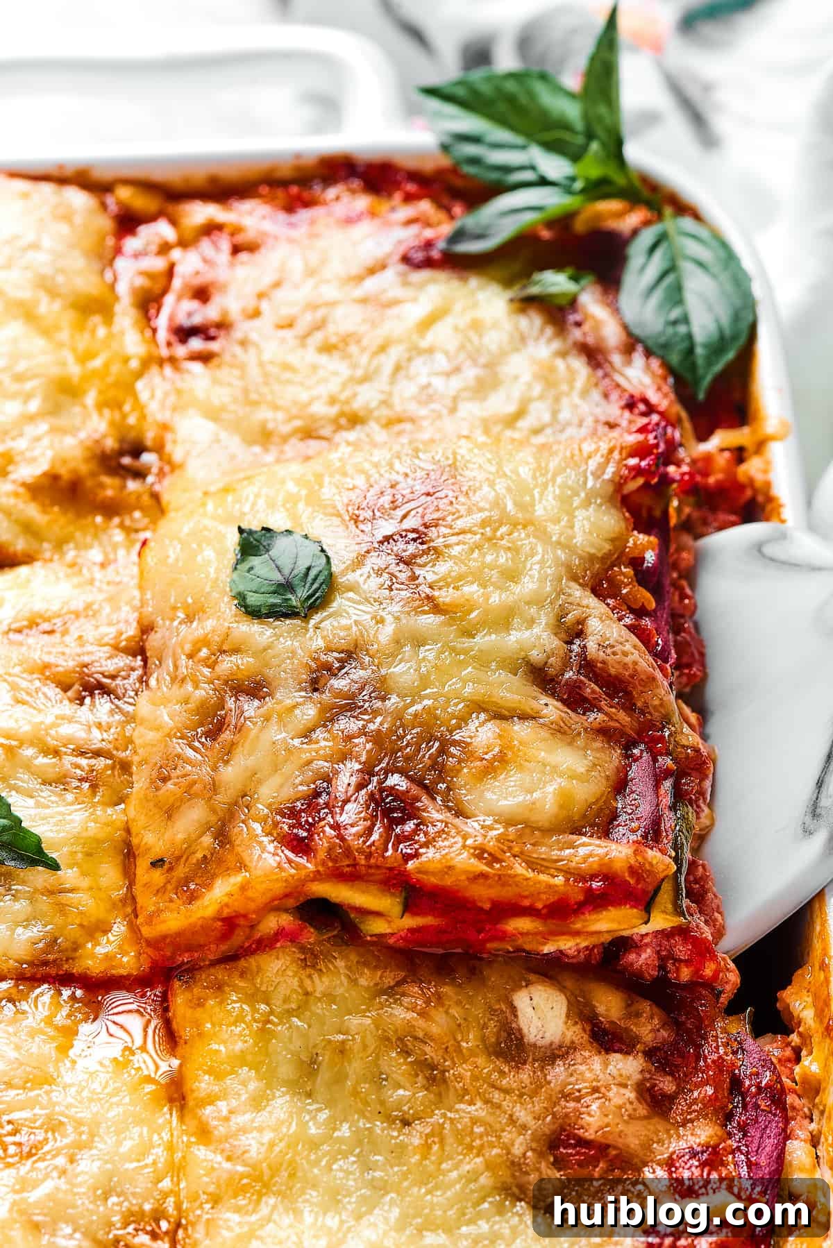 Lasagna being lifted out of a white rectangular baking dish.