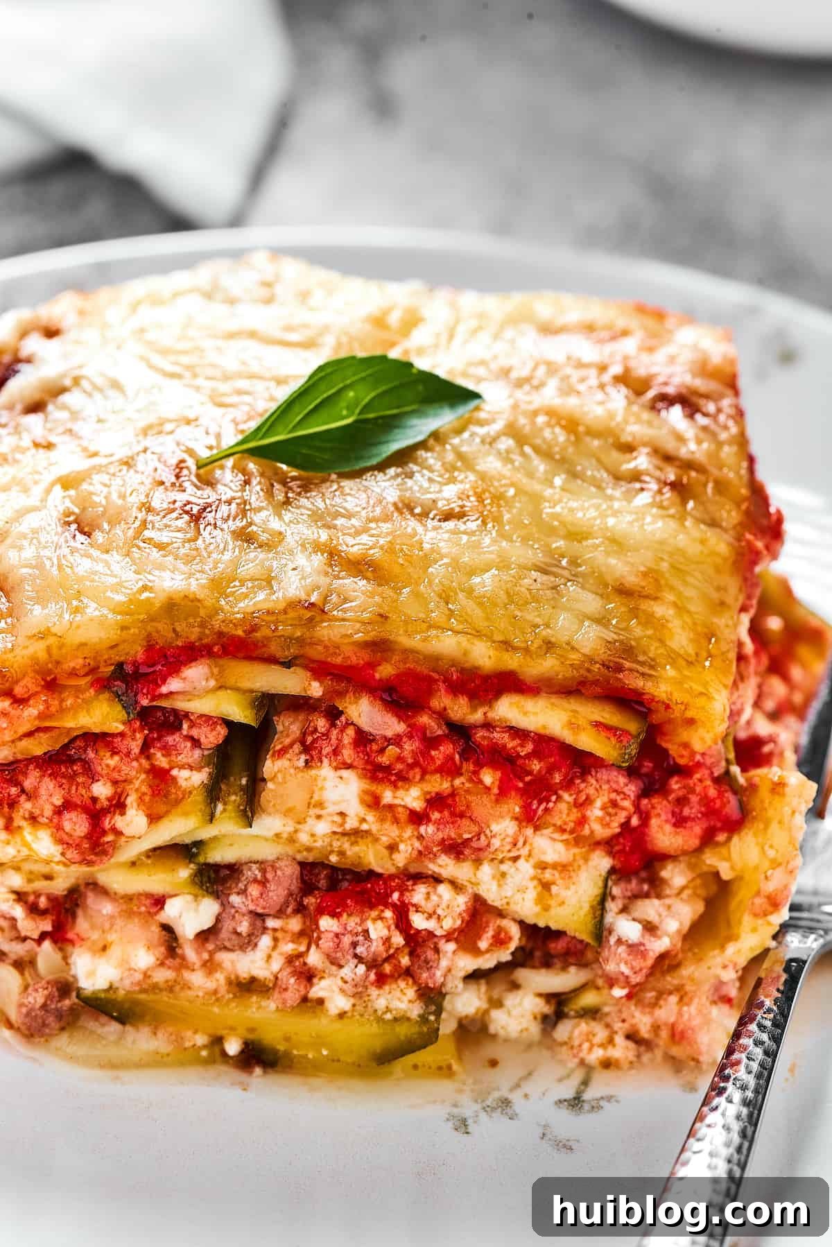 A serving of lasagna on a white dinner plate with a fork.
