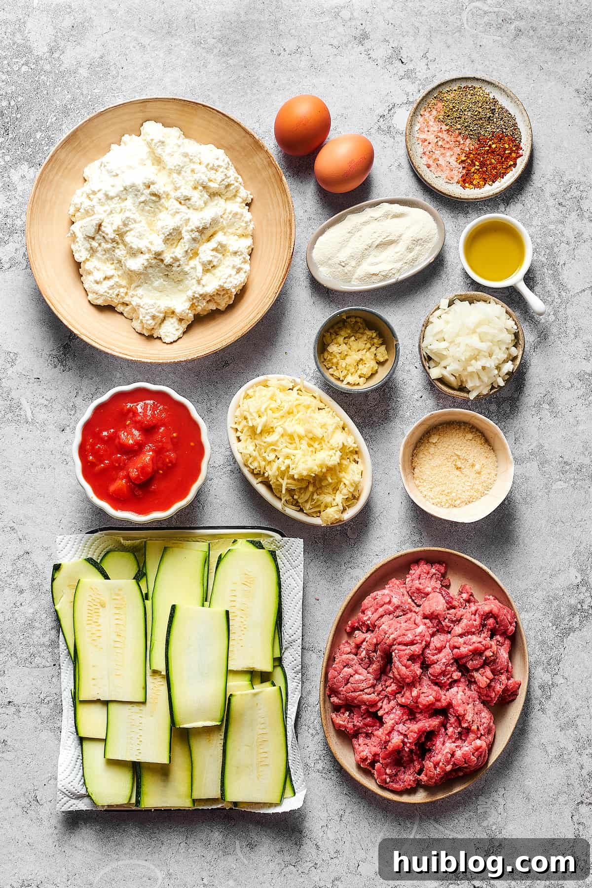 From top left: Cottage cheese, eggs, seasonings, four, olive oil, garlic, diced onion, crushed tomatoes, mozzarella, Parmesan, zucchini slices, ground beef.
