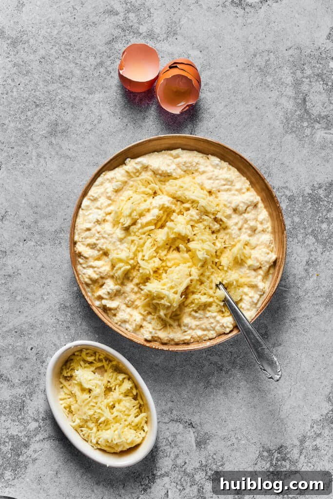Shredded mozzarella added to a large bowl of cheese filling mixture.
