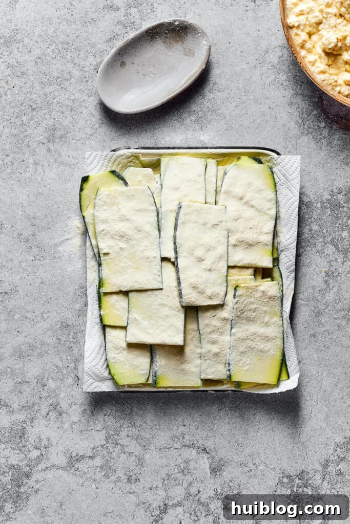 Strips of raw zucchini, lightly-floured and resting on a paper-towel-lined tray.