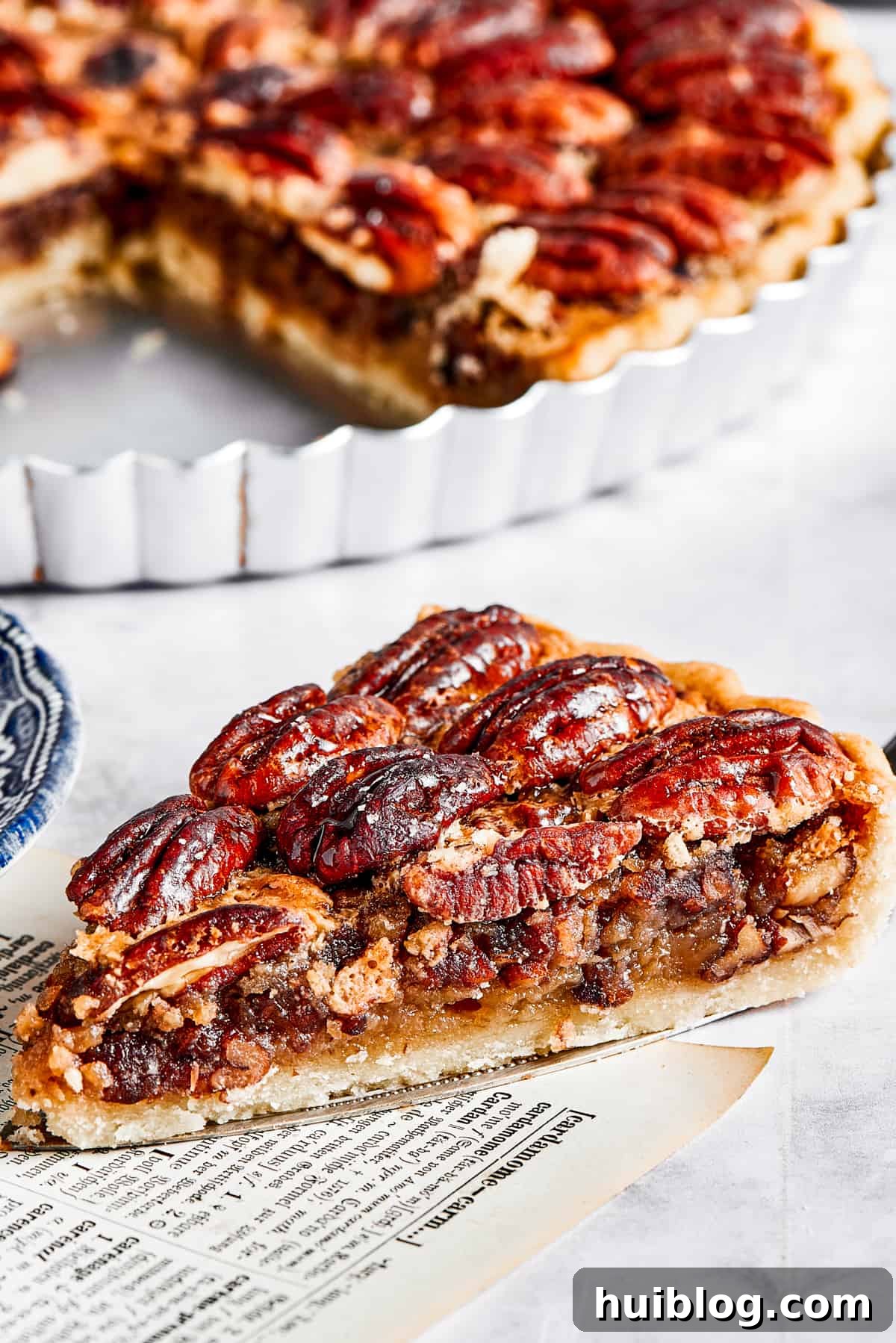 A slice of pie on a pie server, next to the pie dish.