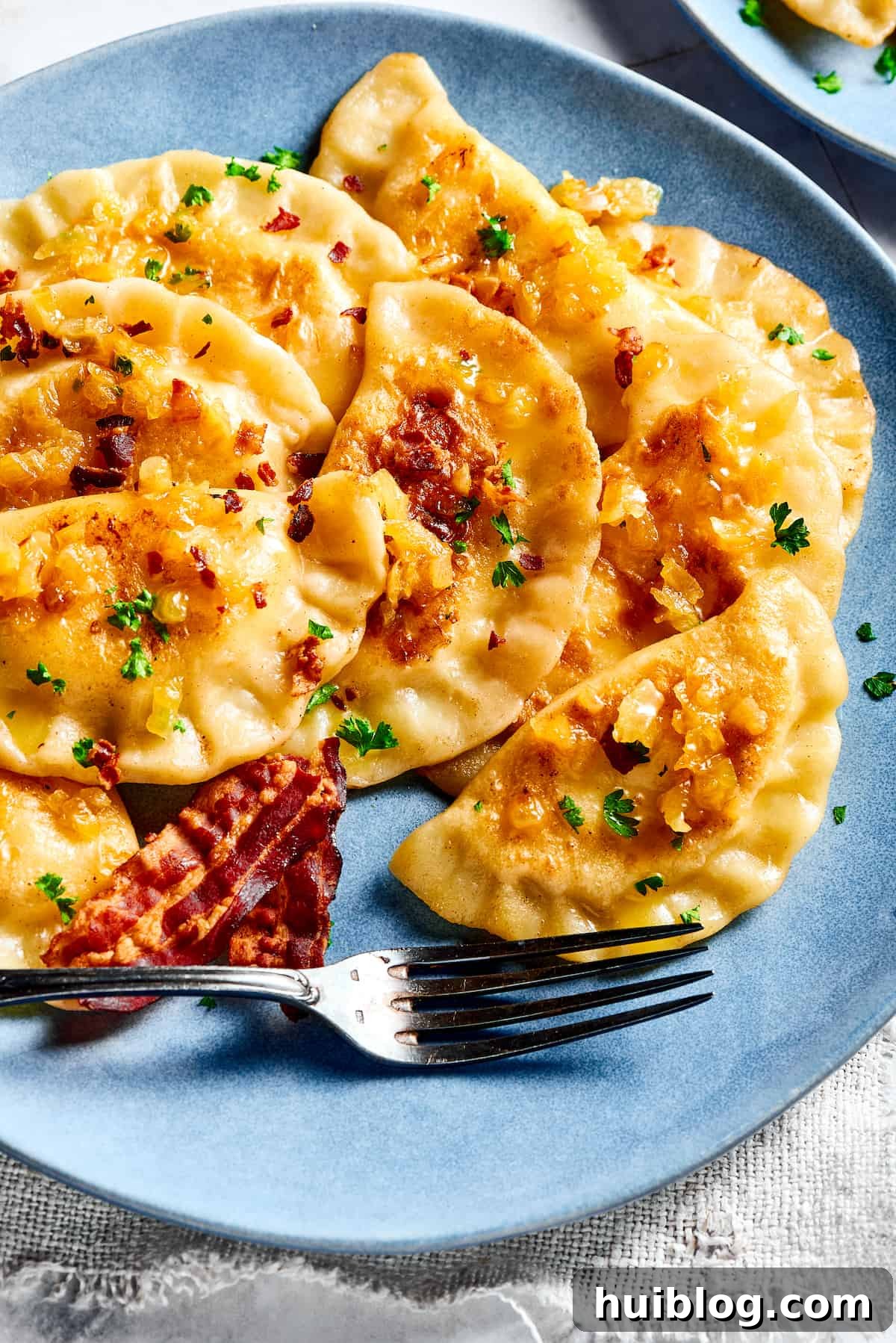 Topped with caramelized onion and crispy bacon, this easy Homemade Pierogi Recipe features a traditional cheese and potato filling. Yum! Bacon and onion topped pierogi ruskie.