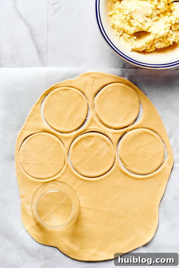 Crafting Perfect Pierogi at Home 6 A sheet of rolled out dough on a work surface, with rounds cut out of it. A bowl of cheesy potato filling is nearby.
