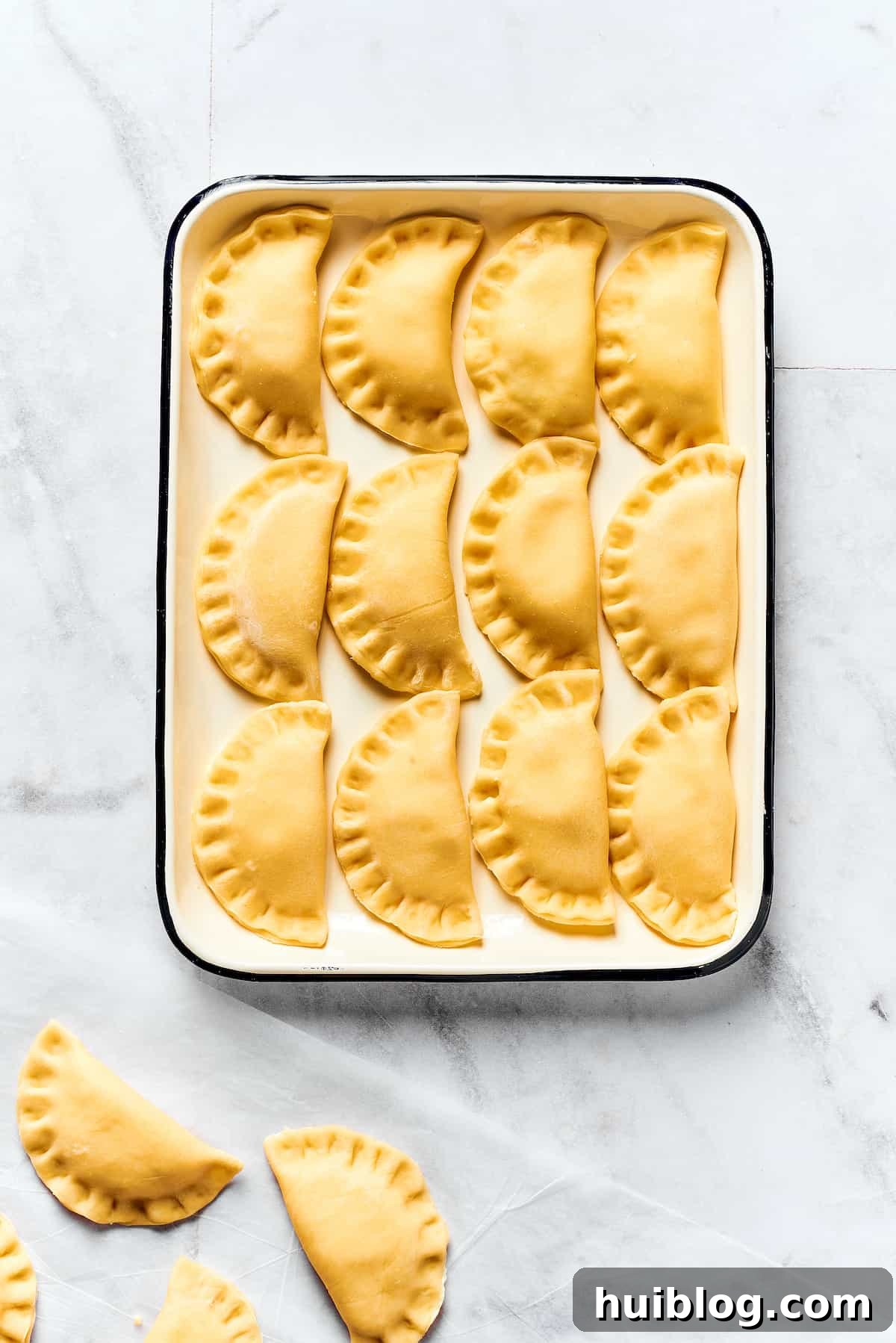Topped with caramelized onion and crispy bacon, this easy Homemade Pierogi Recipe features a traditional cheese and potato filling. Yum! A tray of uncooked pierogies.