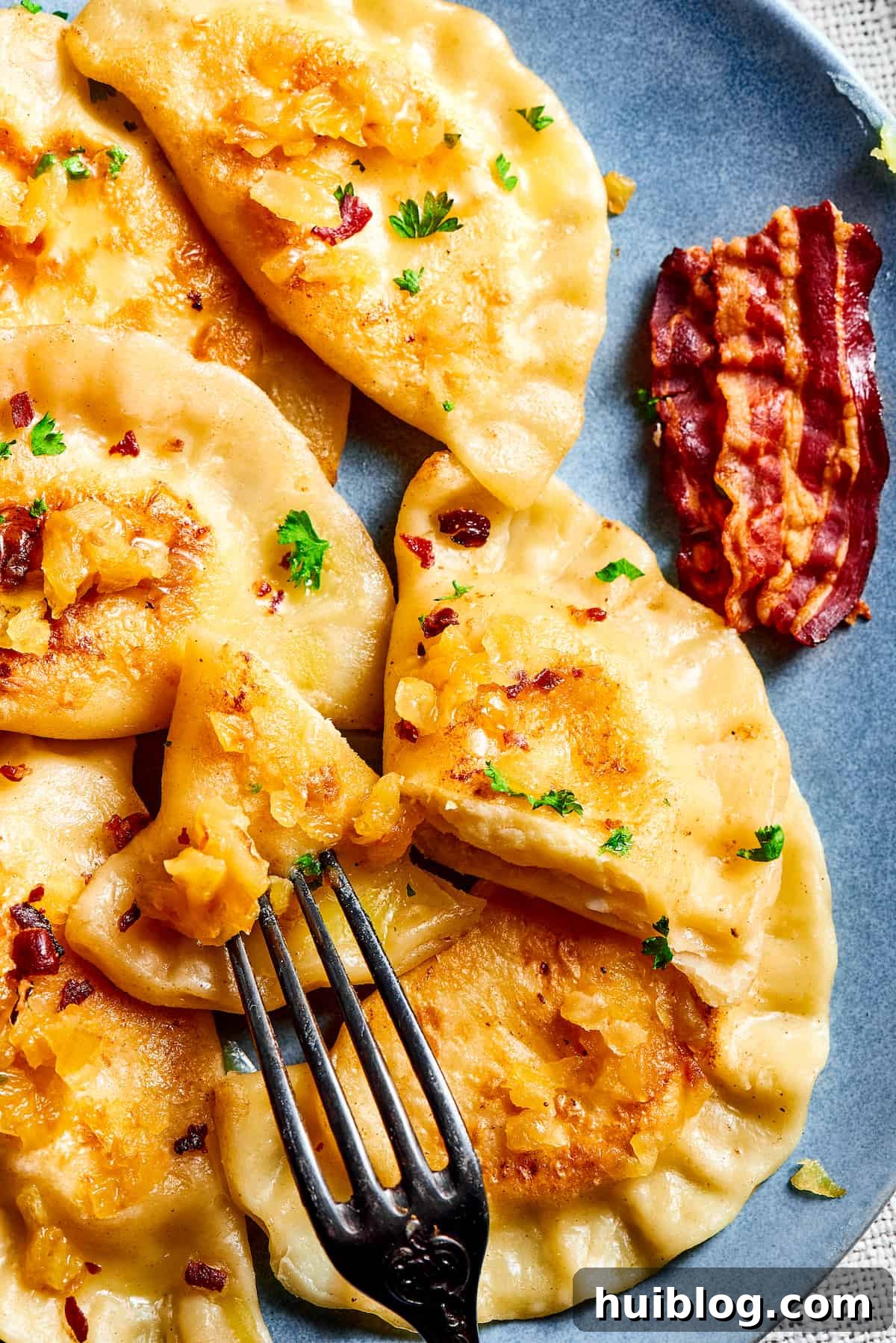 Topped with caramelized onion and crispy bacon, this easy Homemade Pierogi Recipe features a traditional cheese and potato filling. Yum! Cutting into a homemade potato dumpling.