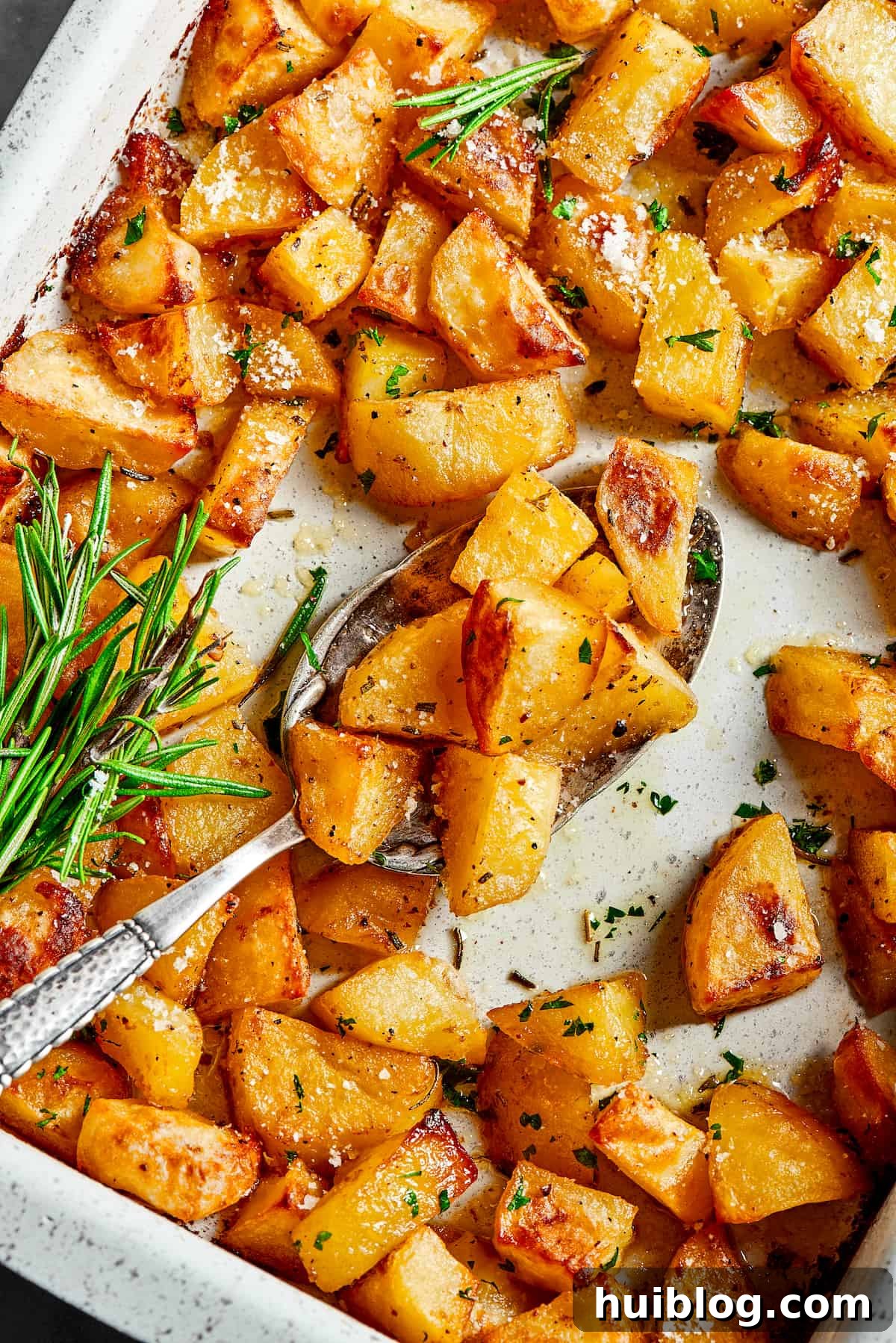 A baking dish with seasoned potatoes, fresh rosemary, and melted butter inside, ready to be roasted.