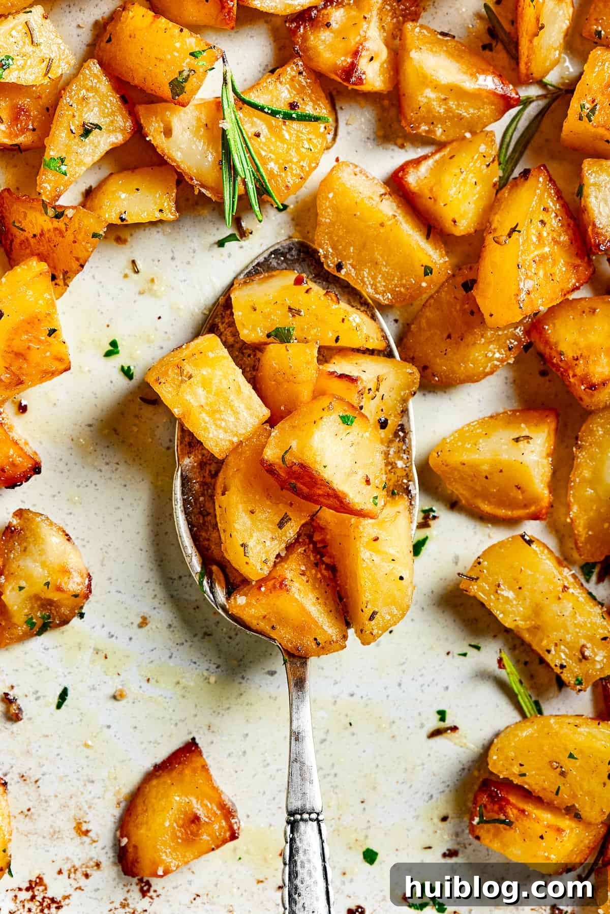 A tray of golden-brown roast potatoes with a silver spoon scooping some pieces, ready to be served.