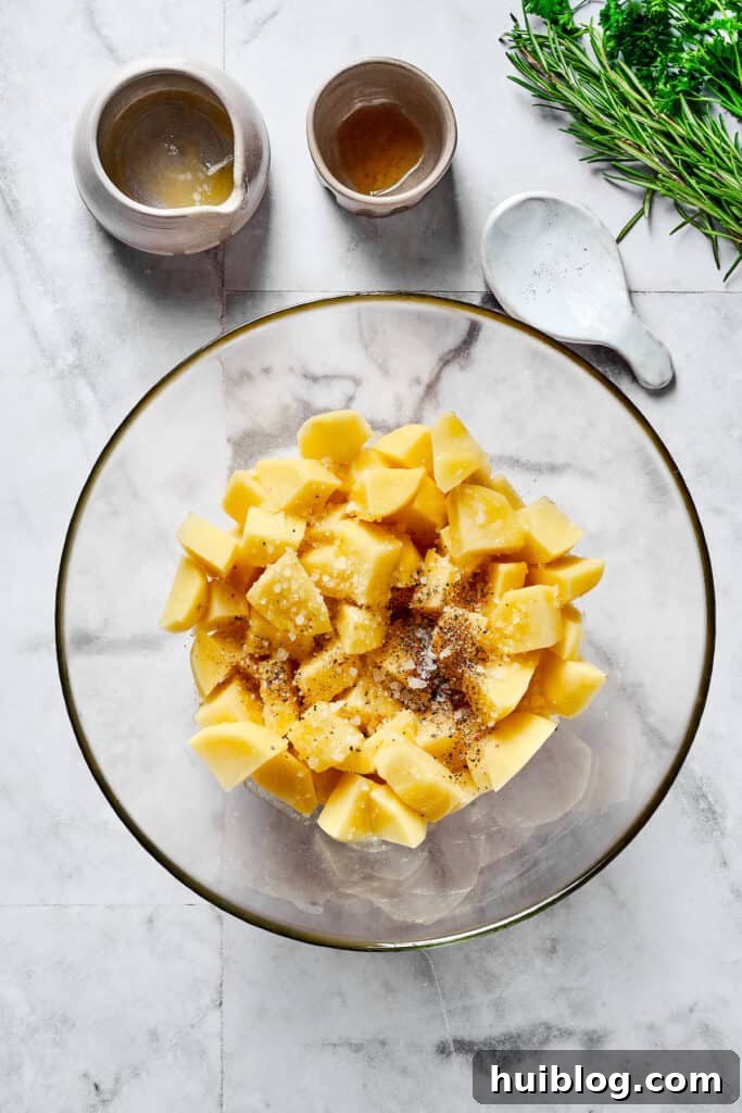 Raw potatoes and seasonings, including rosemary, in a mixing bowl, ready for baking.