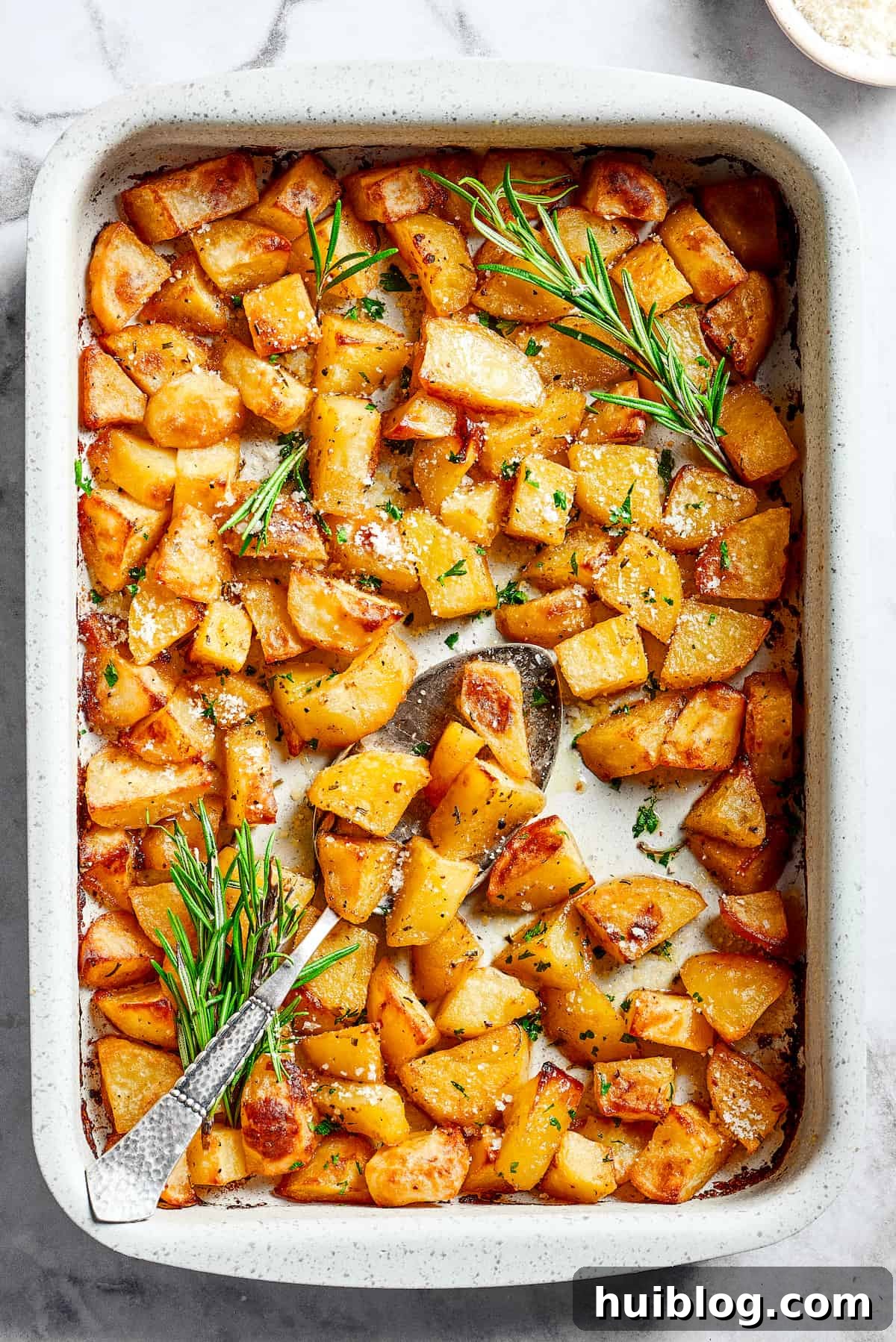 A large baking dish filled with beautifully baked, seasoned potato pieces, hot out of the oven.
