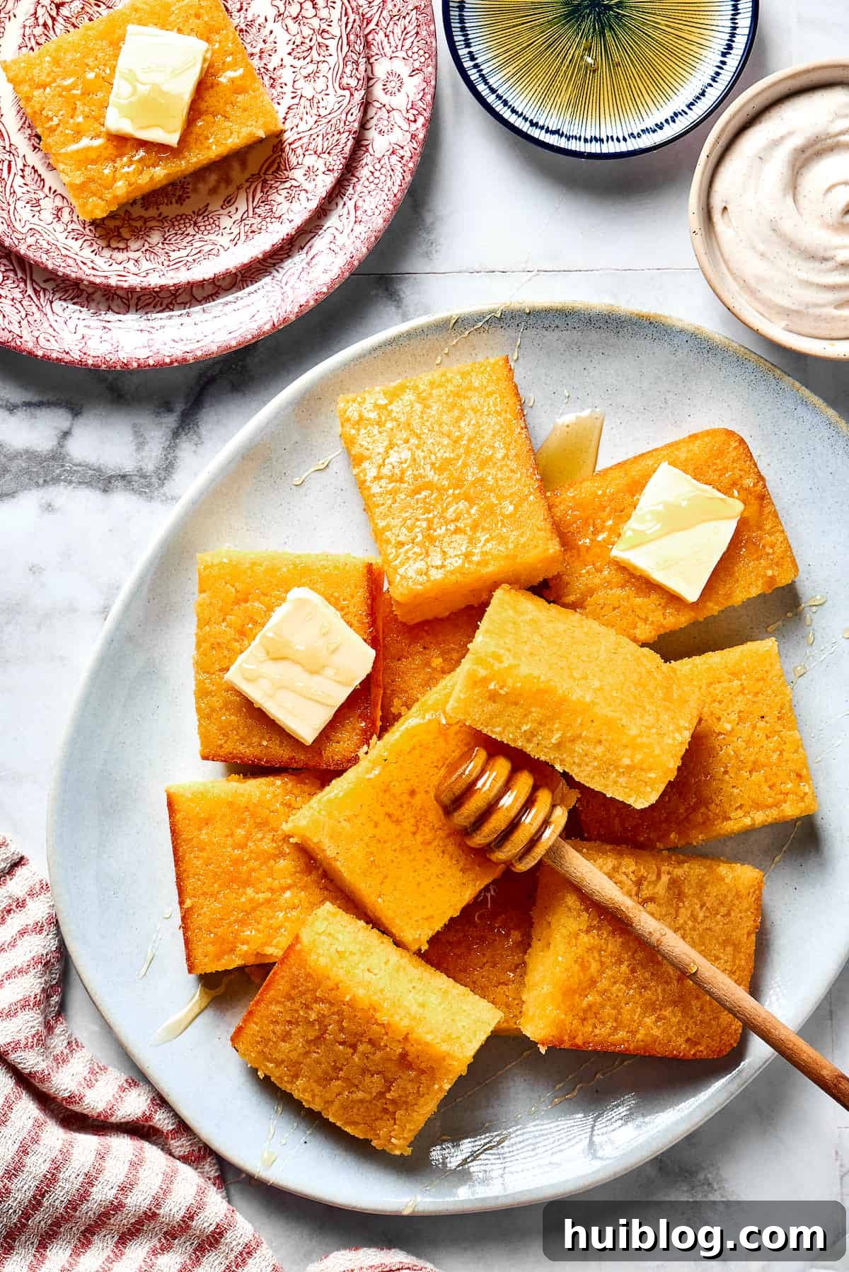 A plate of golden, honey-glazed cornbread squares, accompanied by pats of butter and a honey dipper, showcasing its warm, inviting appeal.