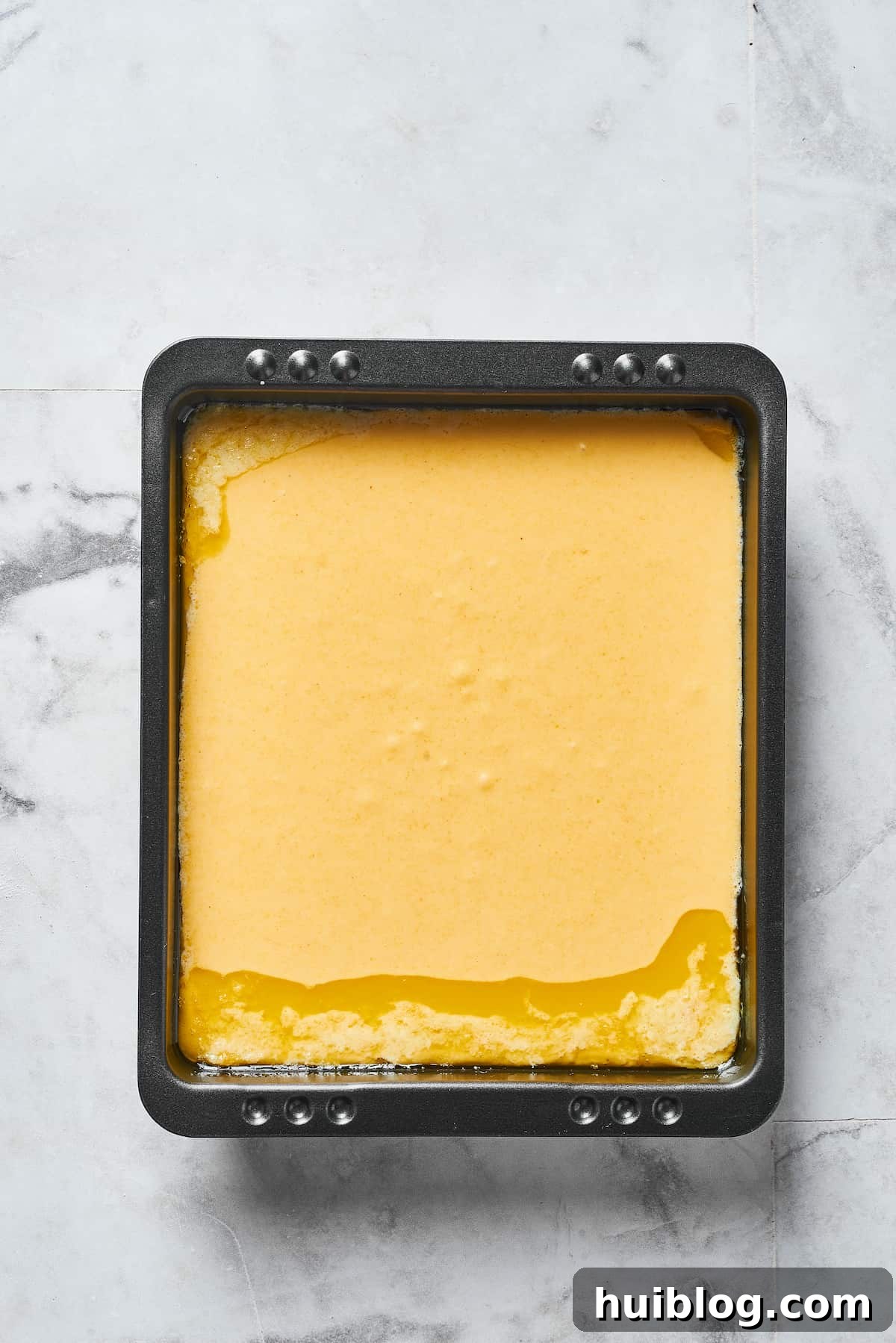 Smooth, golden cornbread batter is poured evenly into a well-greased baking pan, ready for the oven.