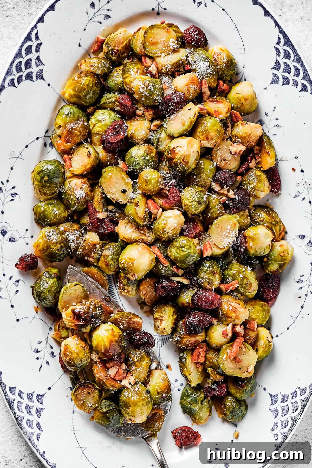 A vibrant close-up of glazed roasted Brussels sprouts adorned with bright red dried cranberries and crunchy chopped pecans, showcasing the glossy glaze and perfect caramelization.