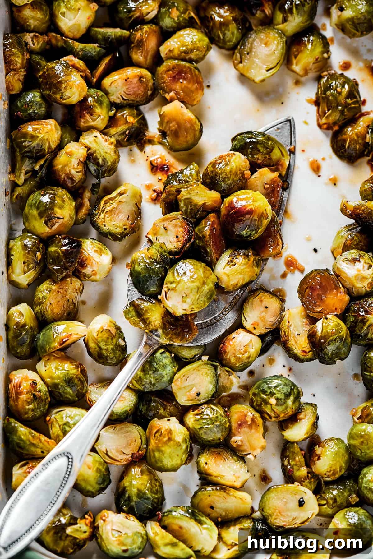 A culinary enthusiast gently tossing freshly roasted Brussels sprouts with a luscious, glossy maple-pomegranate glaze on a baking sheet, ensuring even coating.