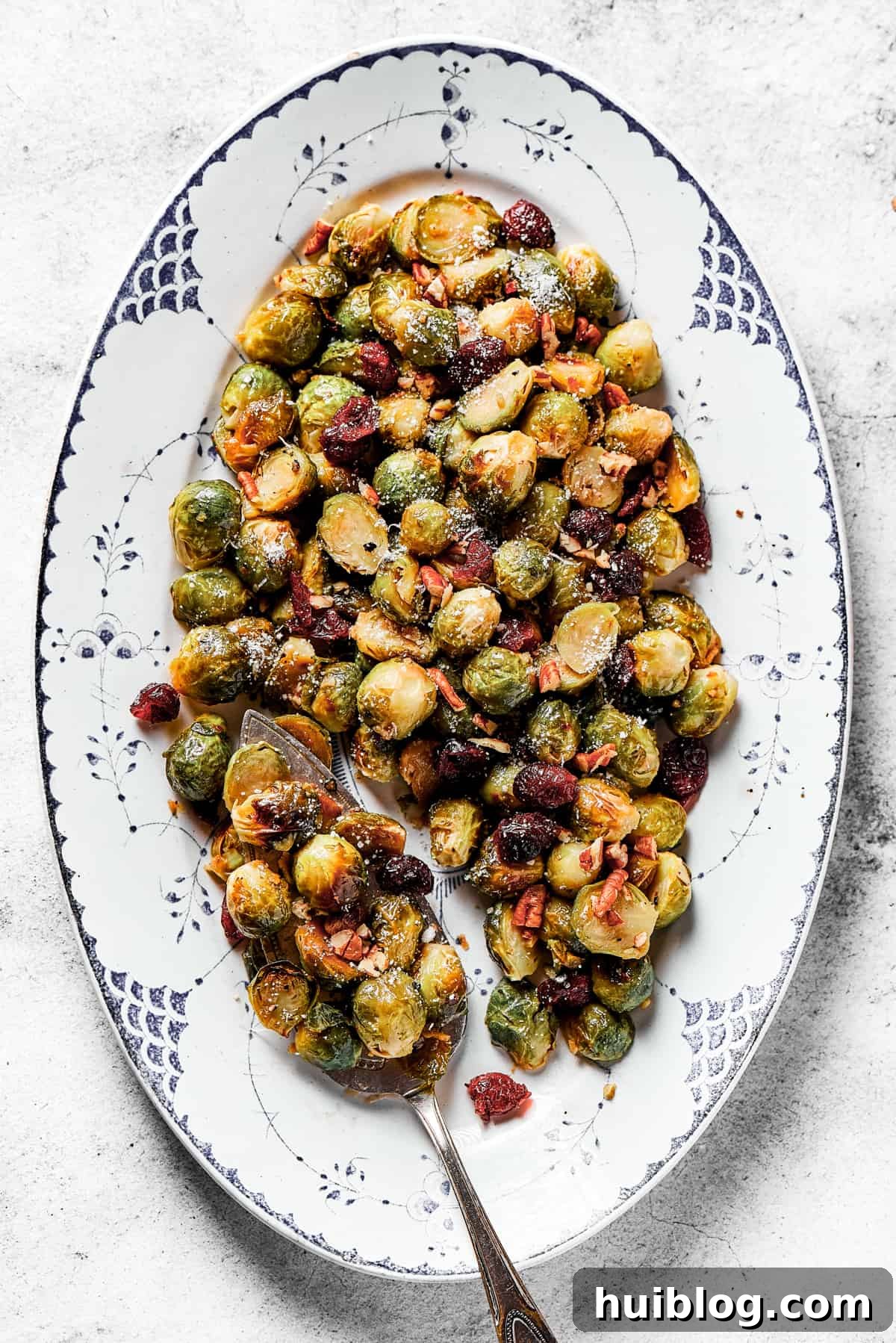 An oval platter generously loaded with golden brown roasted, glazed Brussels sprouts, garnished with cranberries and pecans, ready for serving.