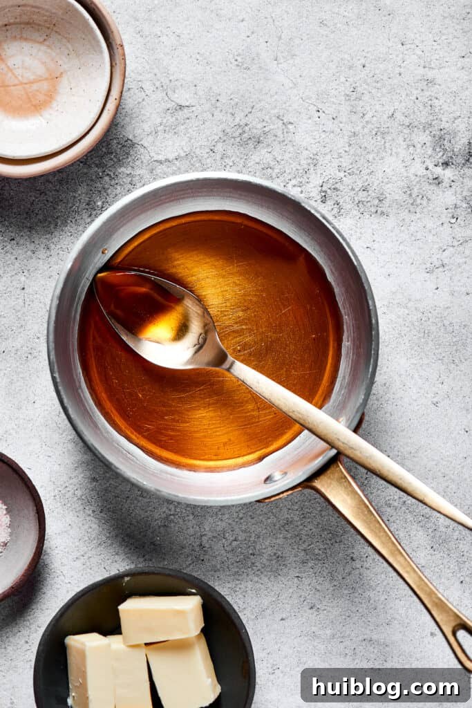 A small saucepan on a stovetop, containing a simmering maple-pomegranate glaze, showing the liquid reducing.