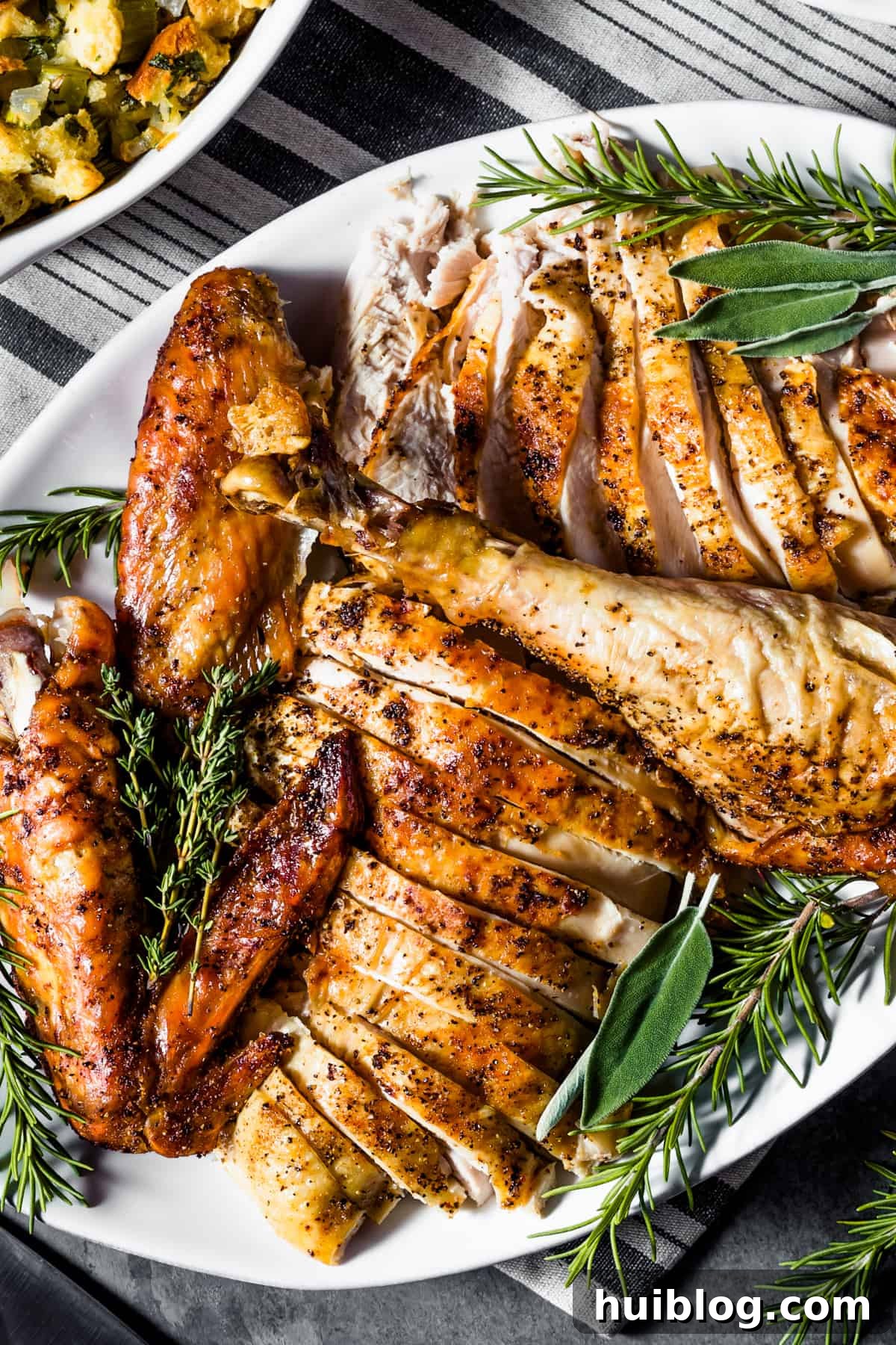 overhead shot of a cut up turkey served on a white oval platter and garnished with fresh herbs.