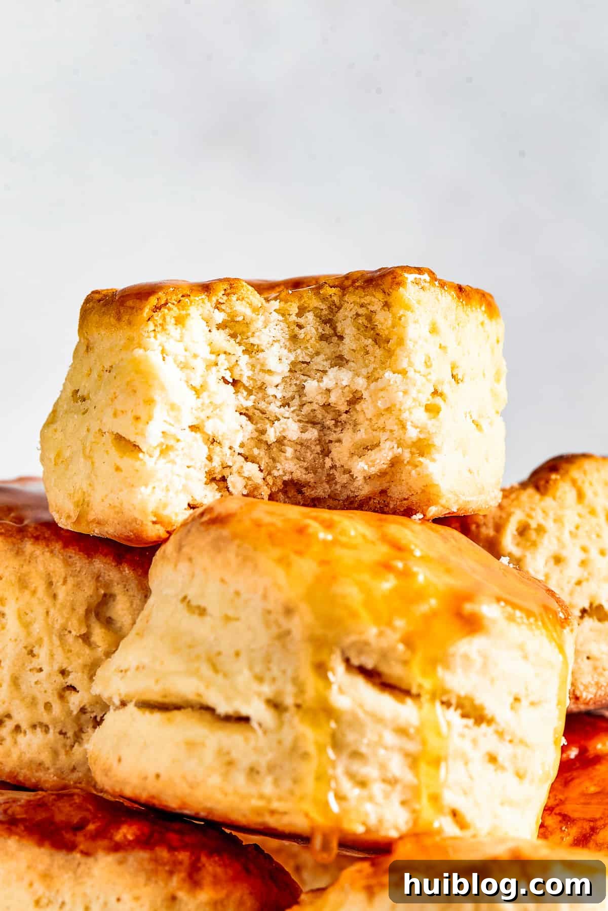 Piled high homemade biscuits on a cake plate, one with a bite taken out, revealing flaky layers.