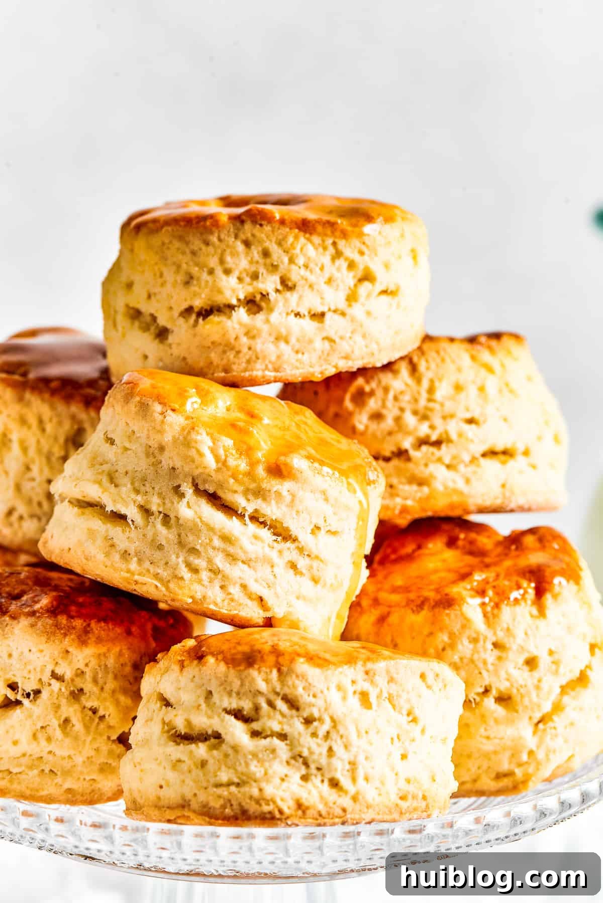 Six golden-brown, fluffy biscuits, elegantly stacked in a pyramid shape on a white cake plate, ready to be enjoyed.