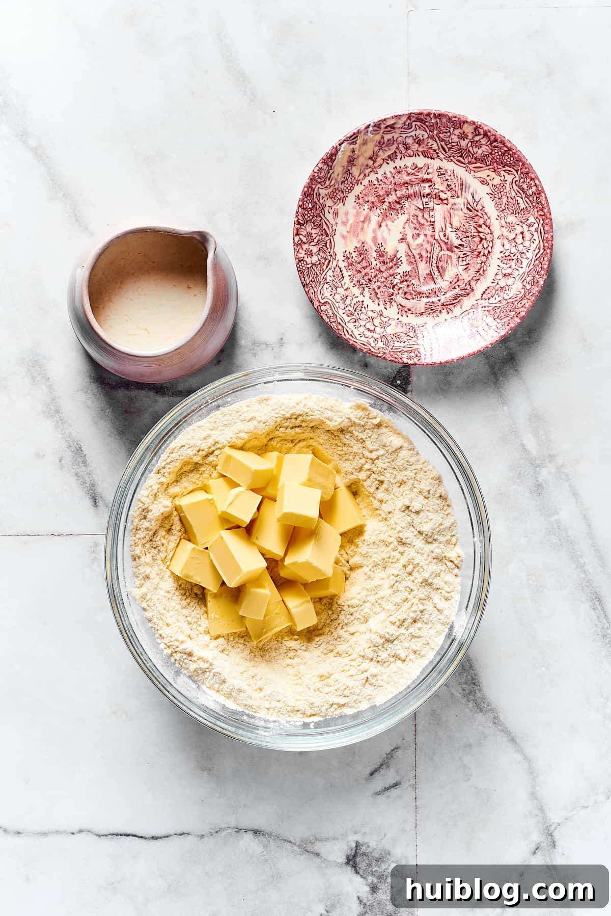 Small cubes of cold butter being added to a mixing bowl containing dry biscuit ingredients.
