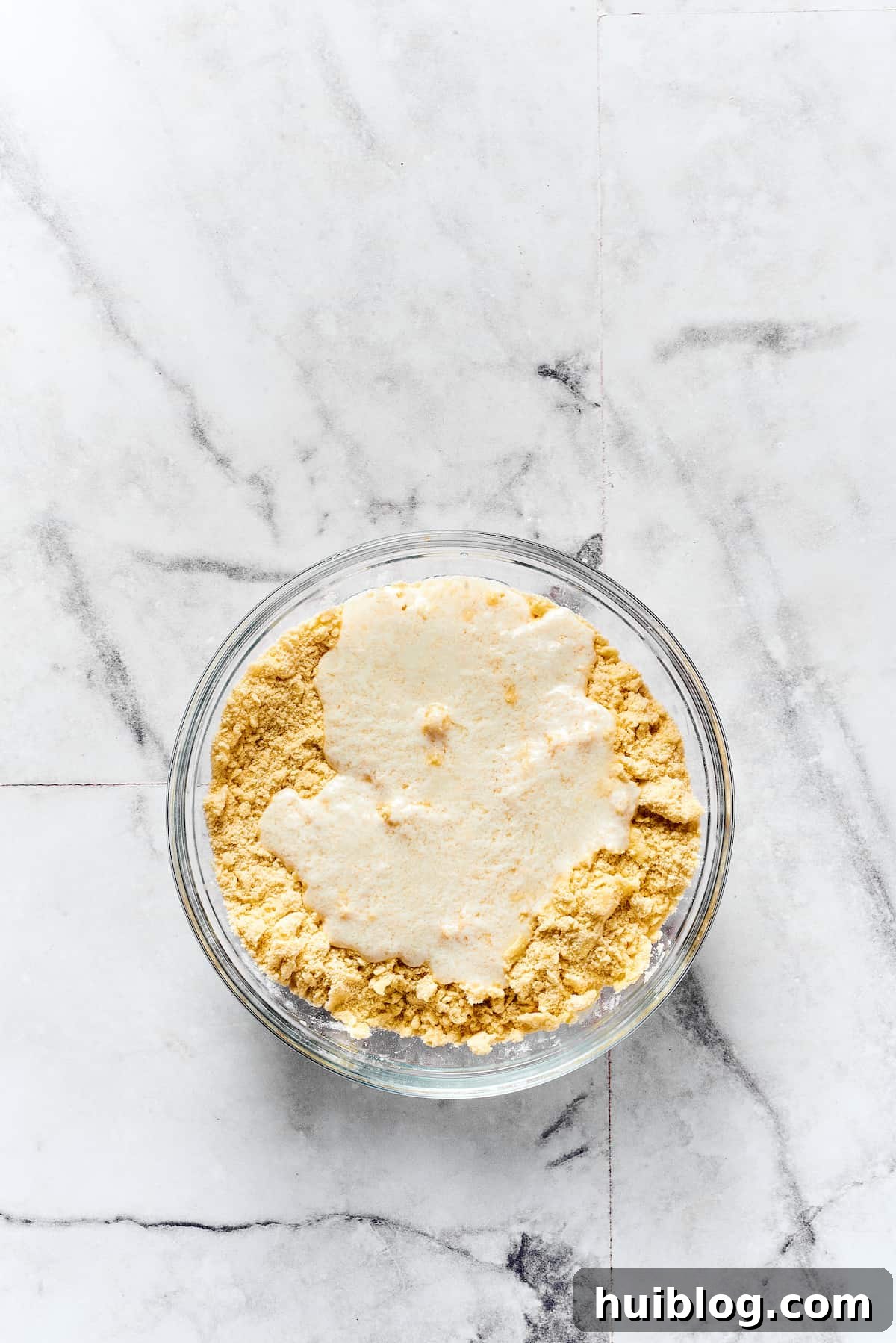Cold buttermilk being carefully mixed into the biscuit dough, creating a soft, shaggy texture.