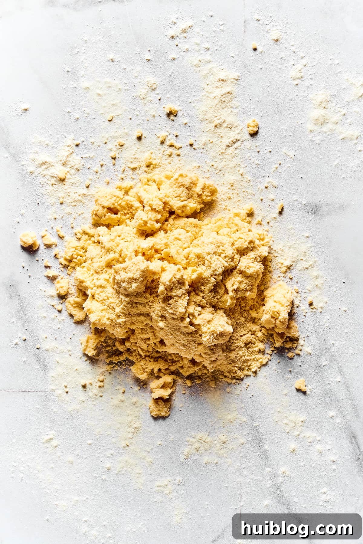 Crumbly, soft biscuit dough resting on a lightly floured marble work surface, prepared for shaping and cutting.