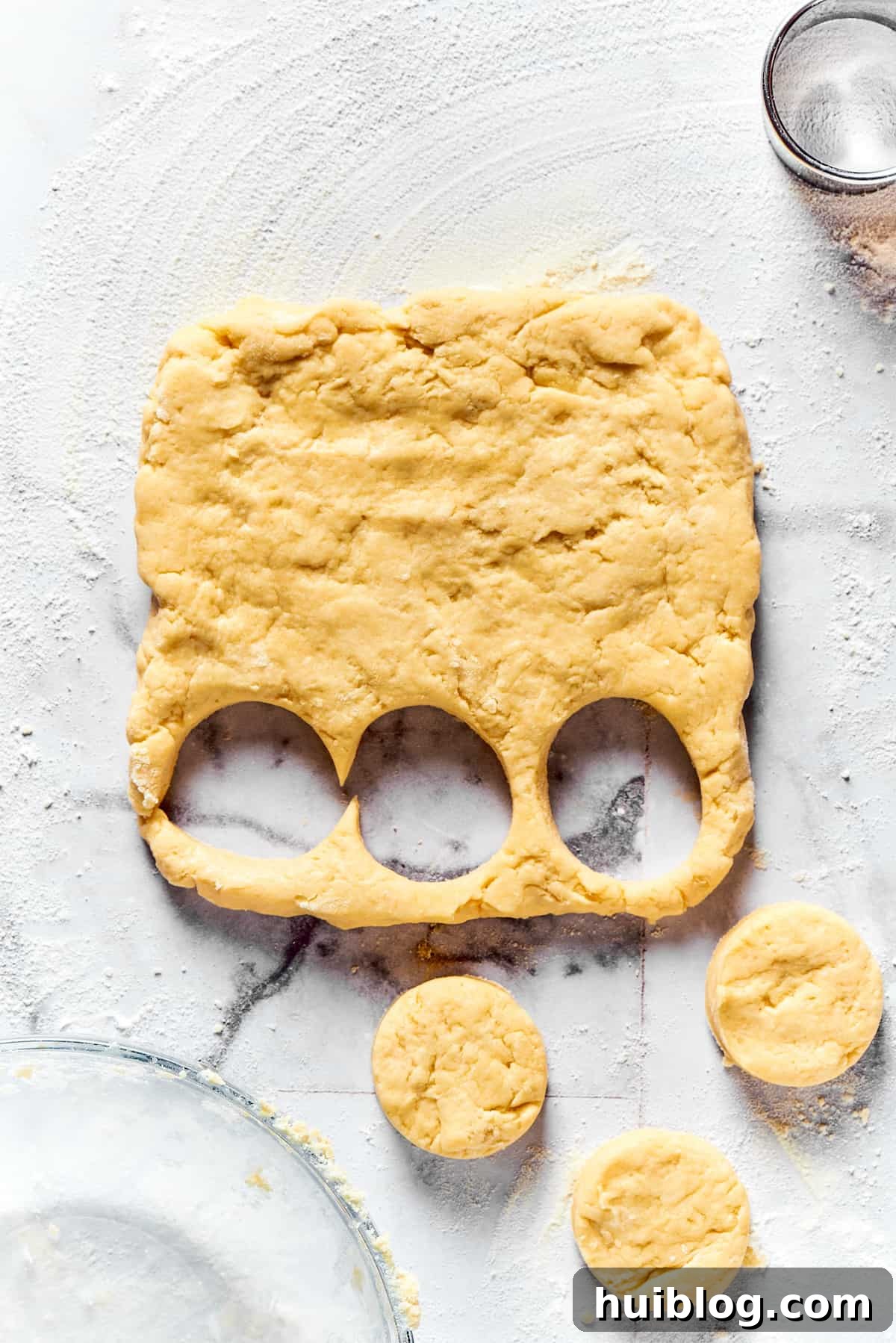 A hand using a biscuit cutter to neatly cut rounds from the flattened biscuit dough.