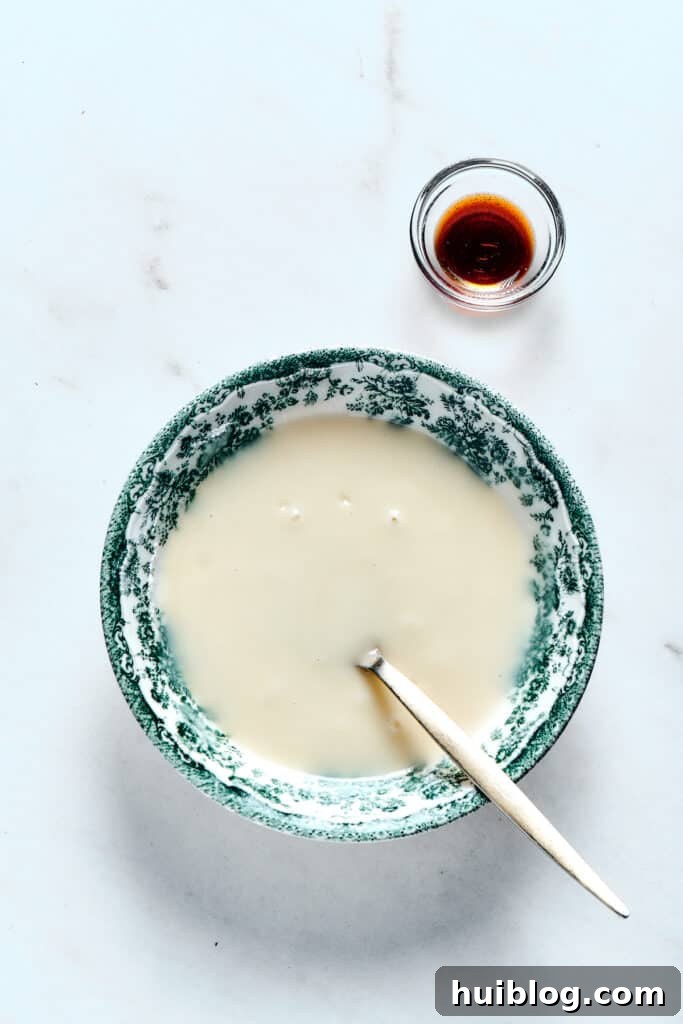 A bowl of creamy orange glaze with a small dish of vanilla paste, a spoon resting in the bowl.