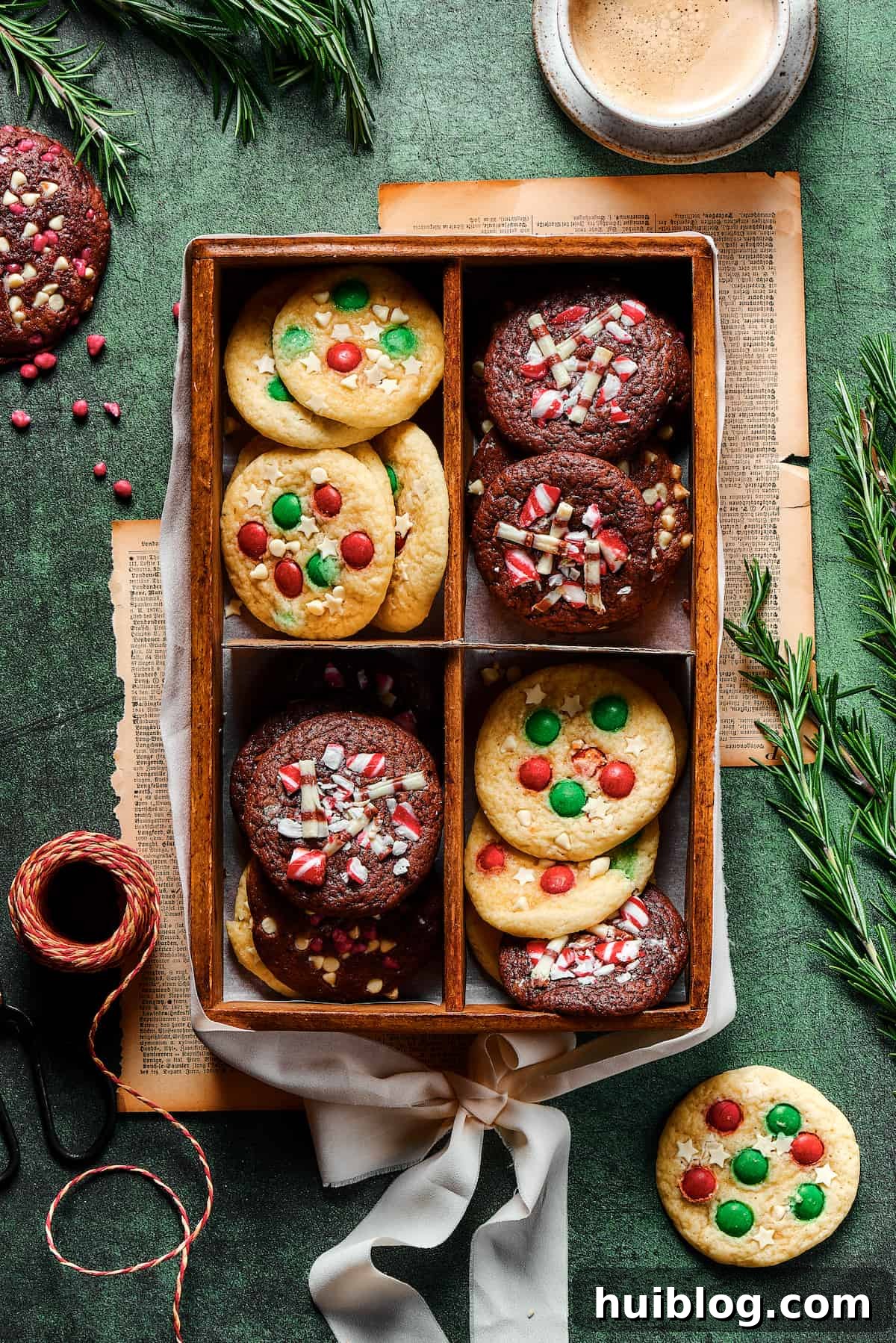 A festive box, divided into four compartments, each filled with a tempting array of freshly baked Christmas cookies, showcasing both vanilla and chocolate varieties adorned with M&Ms and sprinkles.