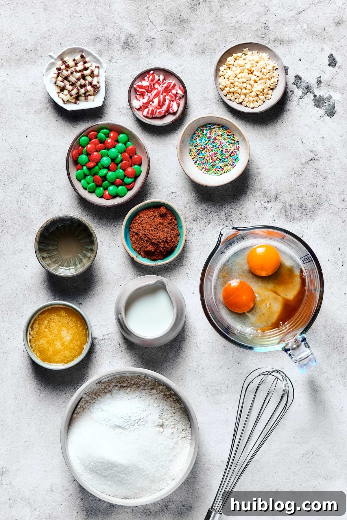 A neatly arranged collection of cake mix cookie ingredients on a rustic wooden table, including a box of cake mix, eggs, butter, milk, and M&Ms, ready for baking festive holiday treats.