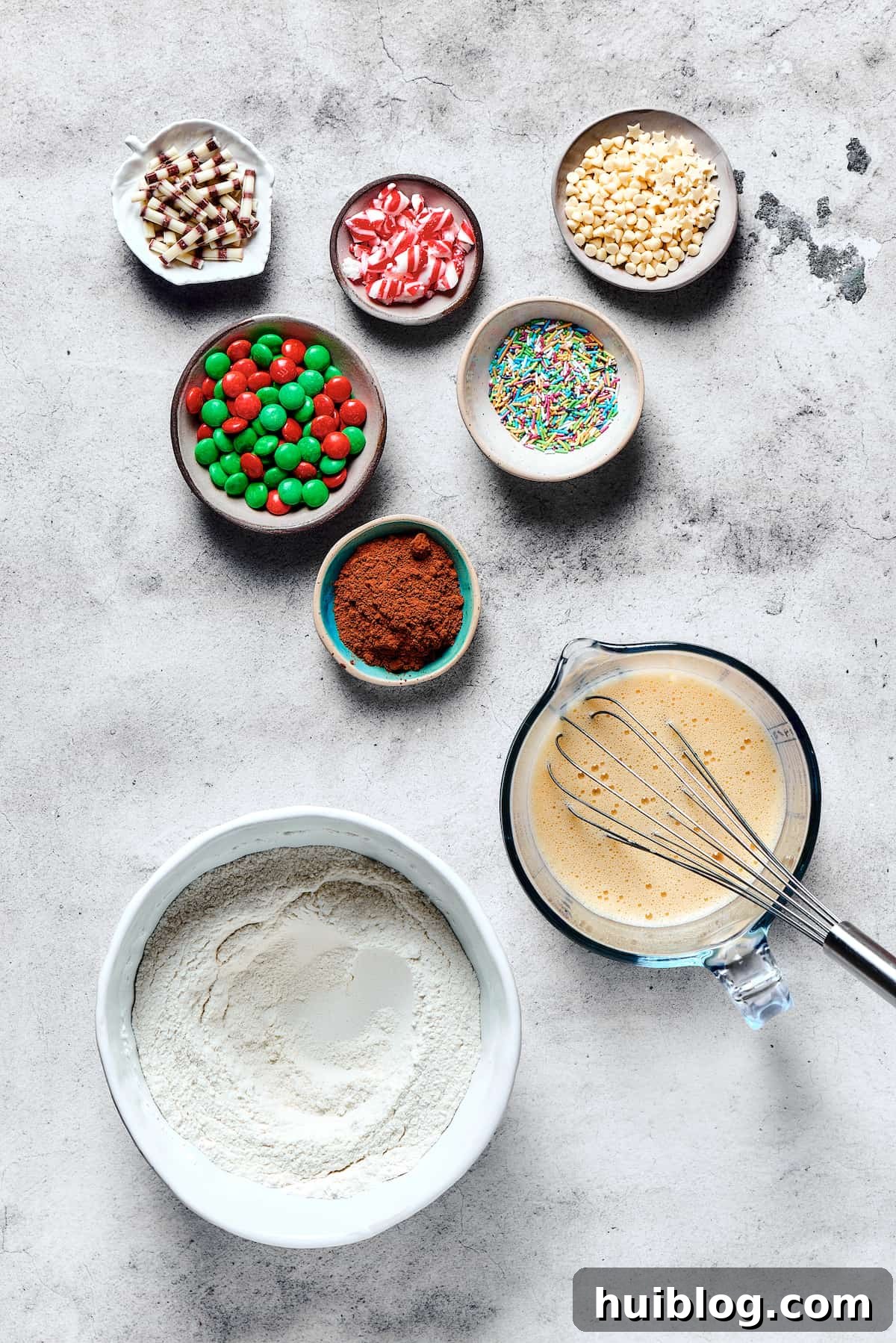 Separate bowls hold the prepared wet and dry ingredients for cake mix cookies, with small dishes of cocoa powder and colorful M&Ms nearby, illustrating the organized prep before mixing.