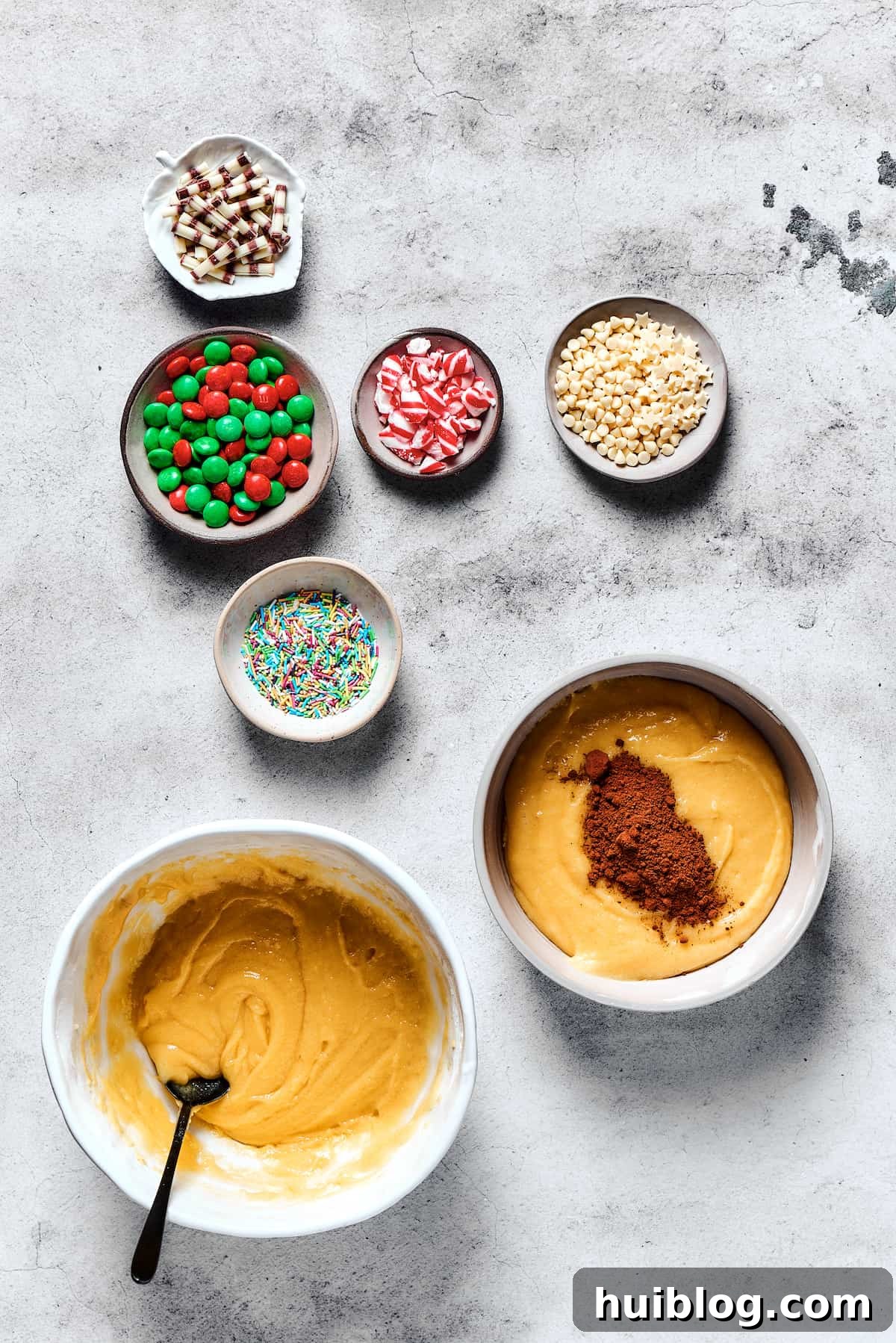 A hand gently folds rich cocoa powder into one half of the prepared cookie dough in a mixing bowl, creating the chocolate base for festive Christmas cookies.