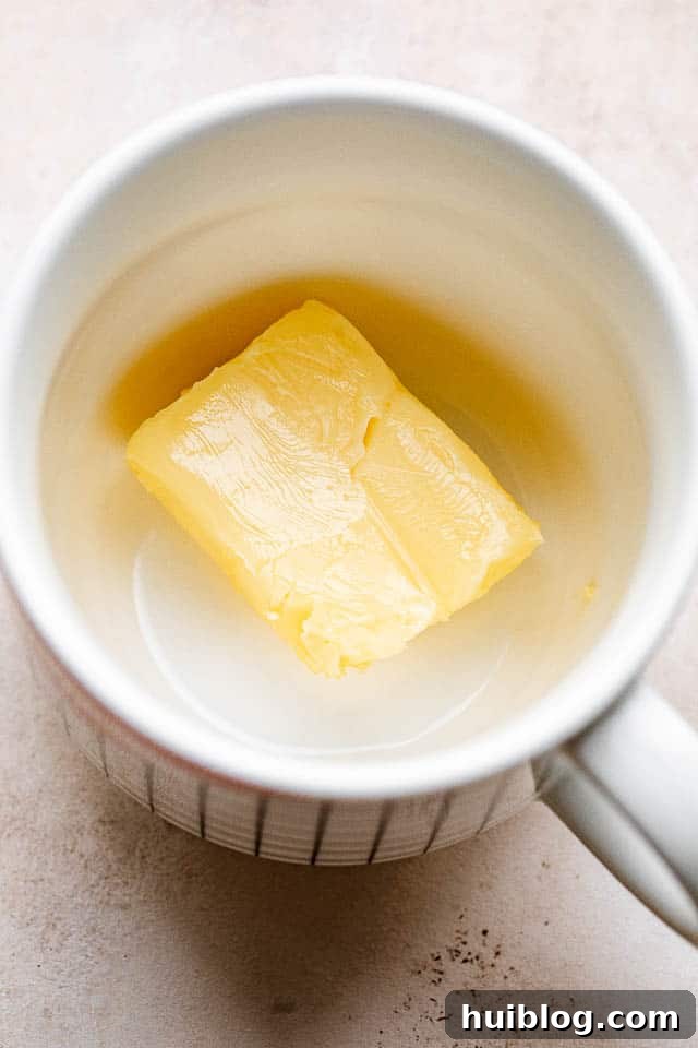 Melted butter glistens at the bottom of a white ceramic mug, ready for mixing.