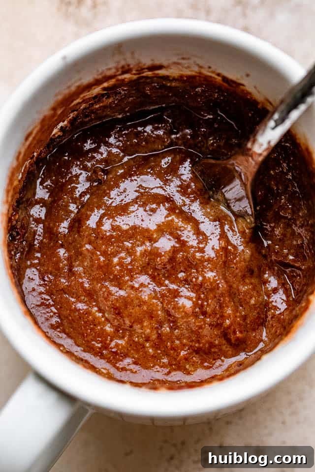 A fork thoroughly mixing a rich, dark chocolate batter inside a mug, showing a smooth consistency.