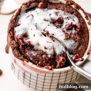 A spoon scooping into a freshly made chocolate mug cake, adorned with fluffy whipped cream and chocolate shavings.