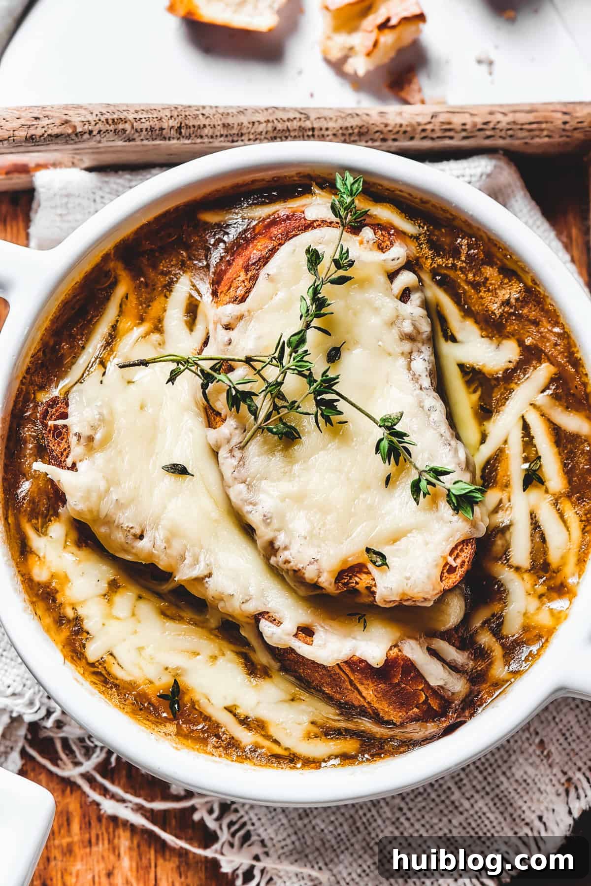 Caramelized Onion & Gruyère Soup 2 A top-down view of a classic French Onion Soup, featuring golden-brown melted cheese over a toasted baguette slice, garnished with fresh thyme sprigs.