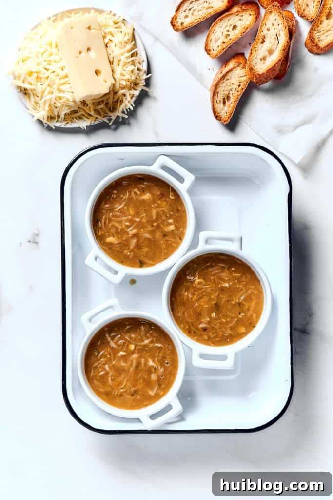 Caramelized Onion & Gruyère Soup 11 Individual oven-proof bowls filled with French onion soup, alongside toasted baguette slices and a bowl of shredded Gruyère and Swiss cheese blend.