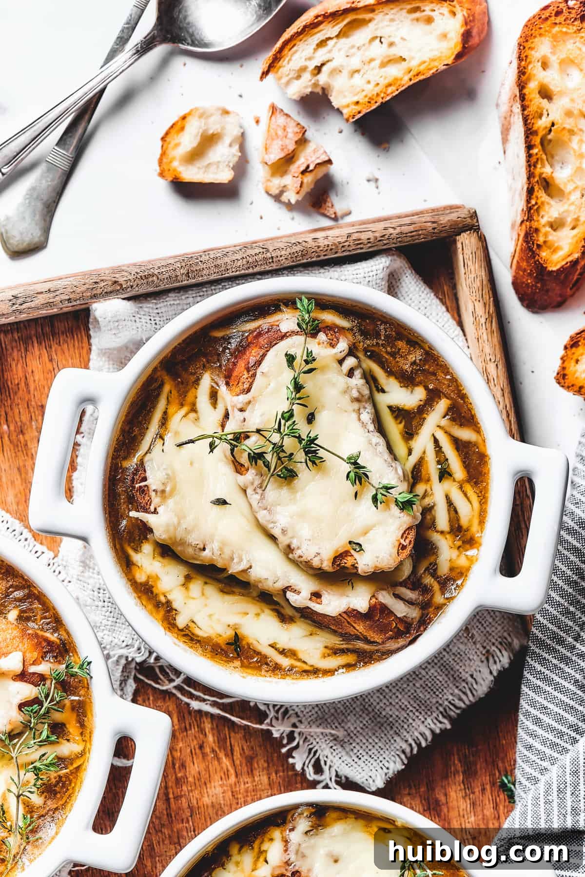 Caramelized Onion & Gruyère Soup 3 Two double-handled ceramic bowls of French onion soup, ready to be served on a rustic wooden tray.