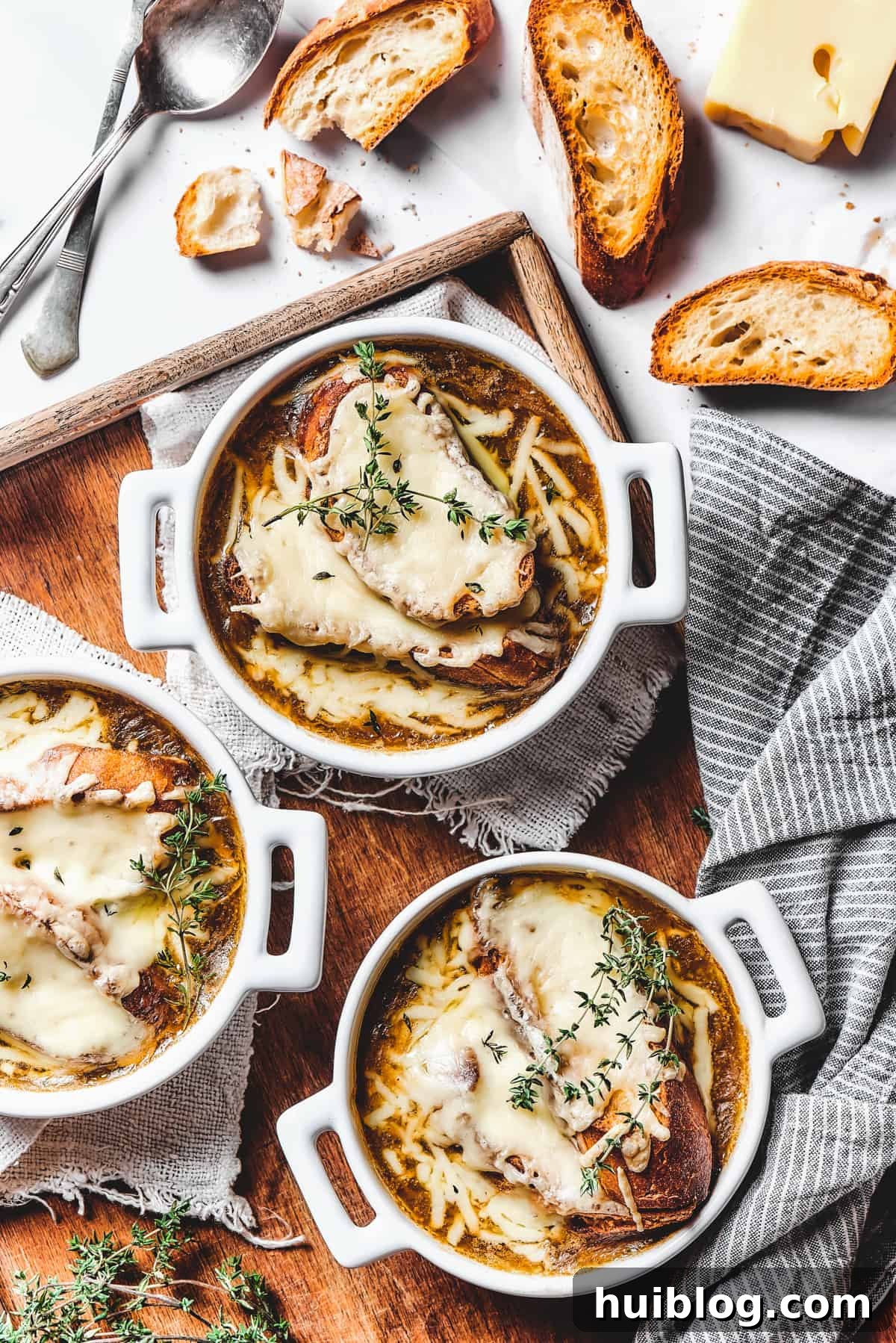 Caramelized Onion & Gruyère Soup 5 Individual serving bowls of French onion soup, each crowned with a generous layer of melted cheese and a golden crouton, ready to be enjoyed.