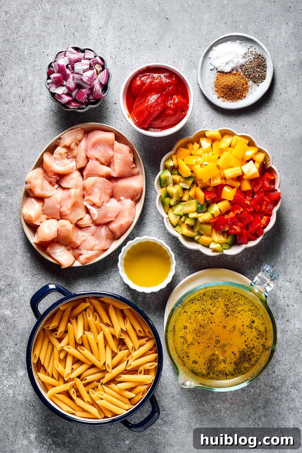 Chicken fajita pasta ingredients neatly arranged in small bowls on a wooden countertop, showcasing colorful vegetables, chicken, pasta, and seasonings.