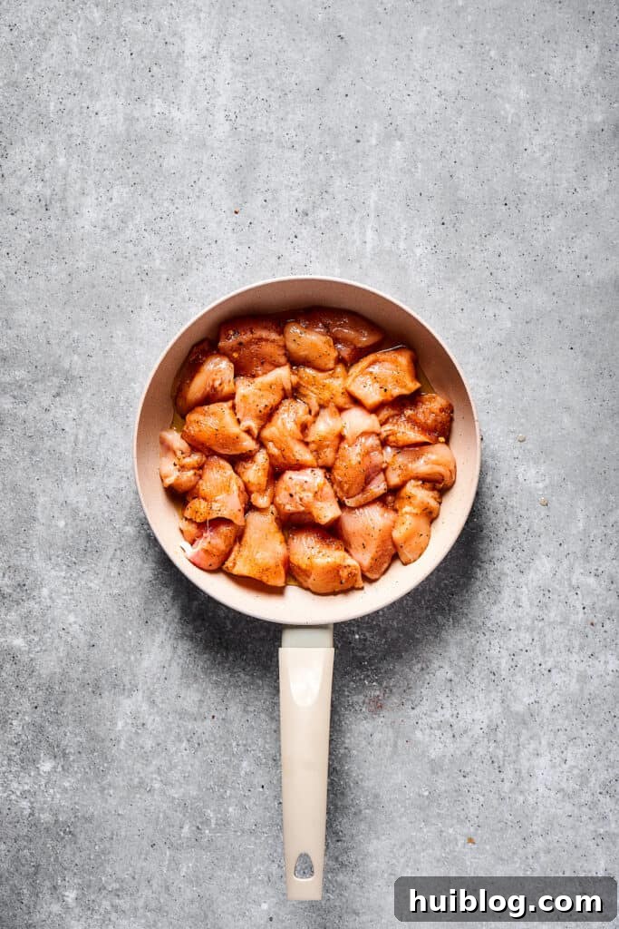 Bite-sized raw chicken pieces seasoned and ready to cook in a large skillet, glistening with olive oil.