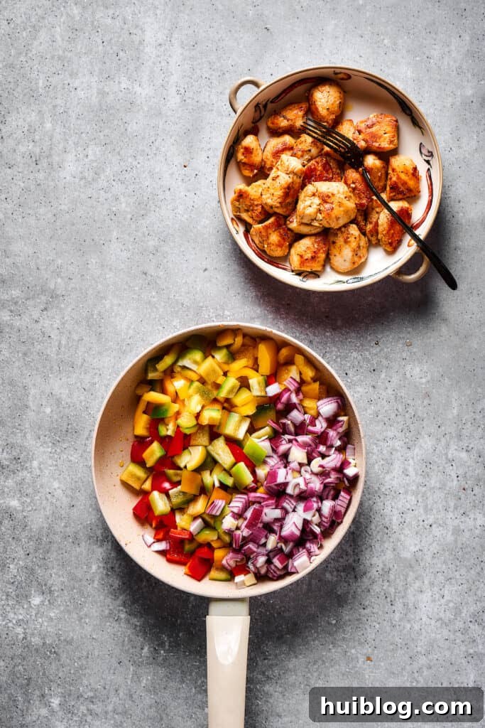 Sautéed diced onions and colorful bell peppers in a skillet, next to a plate of already cooked chicken pieces.