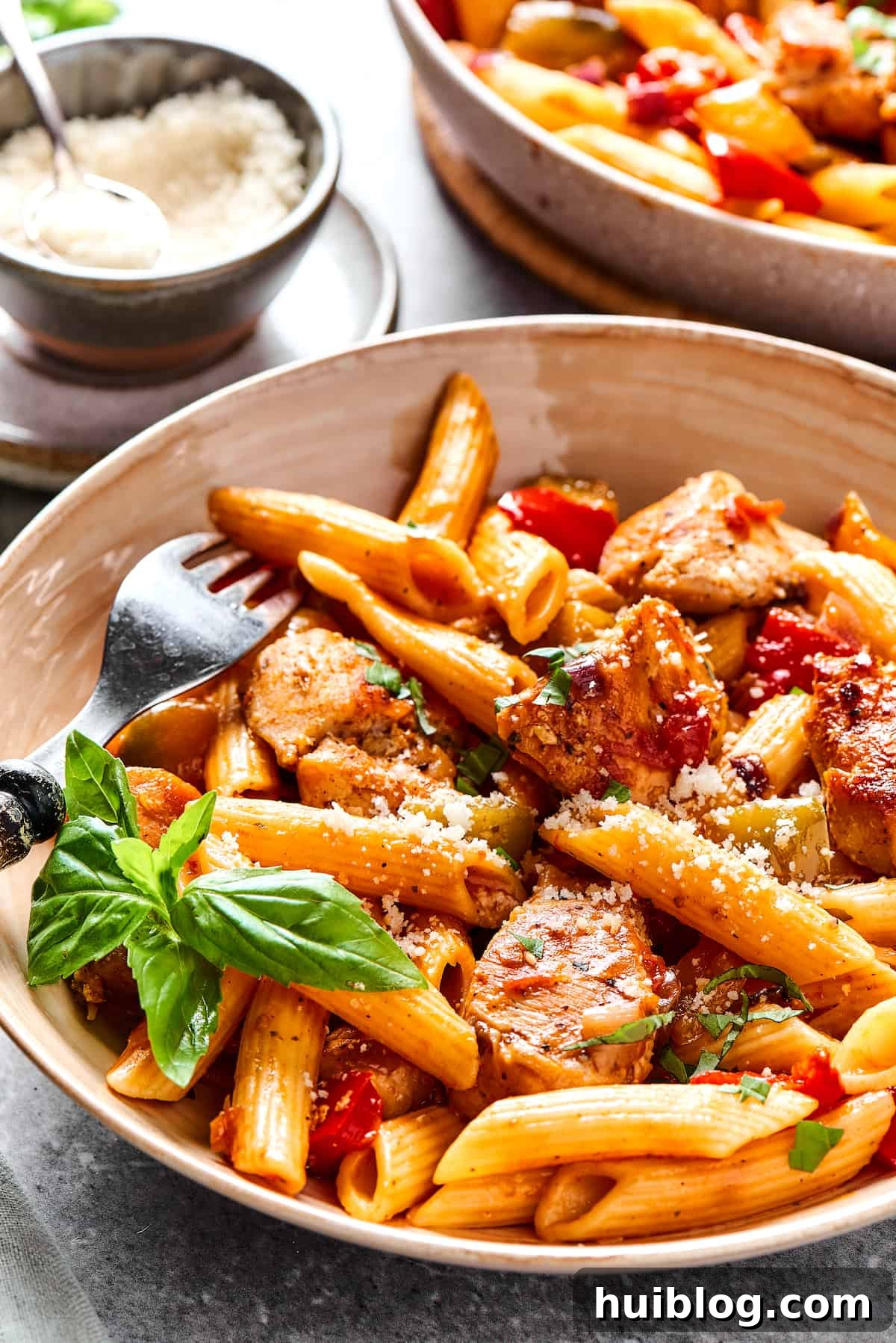 A large skillet filled with cooked penne pasta, vibrant bell peppers, onions, and seasoned chicken, ready to be served.