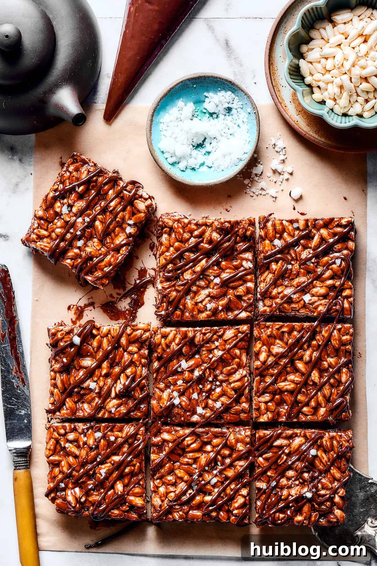 Experience the perfect blend of light crunch and chewy marshmallow, enhanced by rich dark chocolate in these easy-to-make treats. Squares of chocolate rice krispie treats next to a bowl of flaky sea salt, showcasing their delightful texture and rich color.