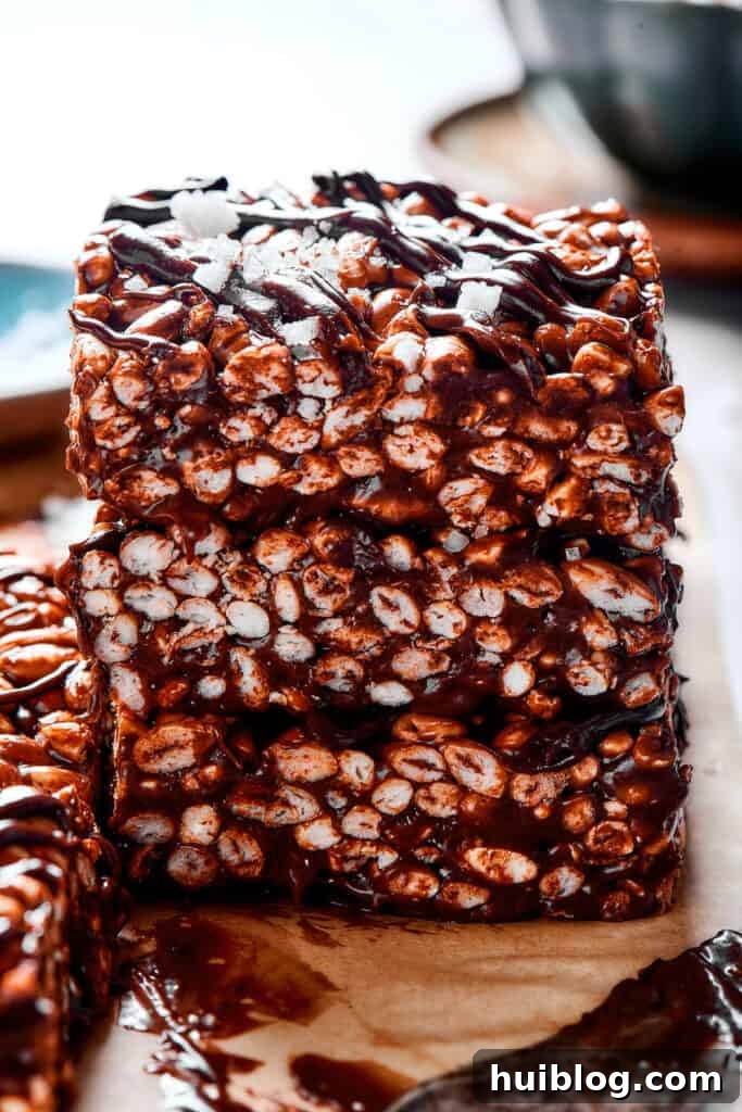 No-Bake Chocolate Crispy Treats 9 A stack of perfectly cut chocolate rice krispie treats, each square adorned with a rich chocolate drizzle, ready to be enjoyed.