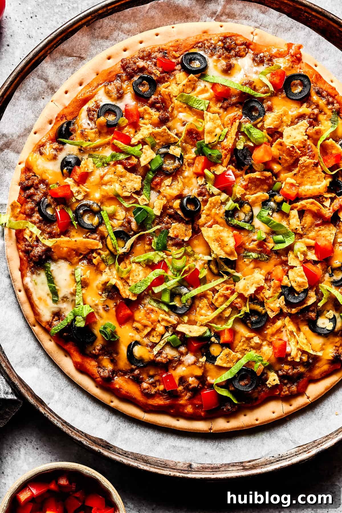A perfectly baked taco pizza, richly topped with fresh diced tomatoes, green onions, and shredded lettuce, ready to be served.