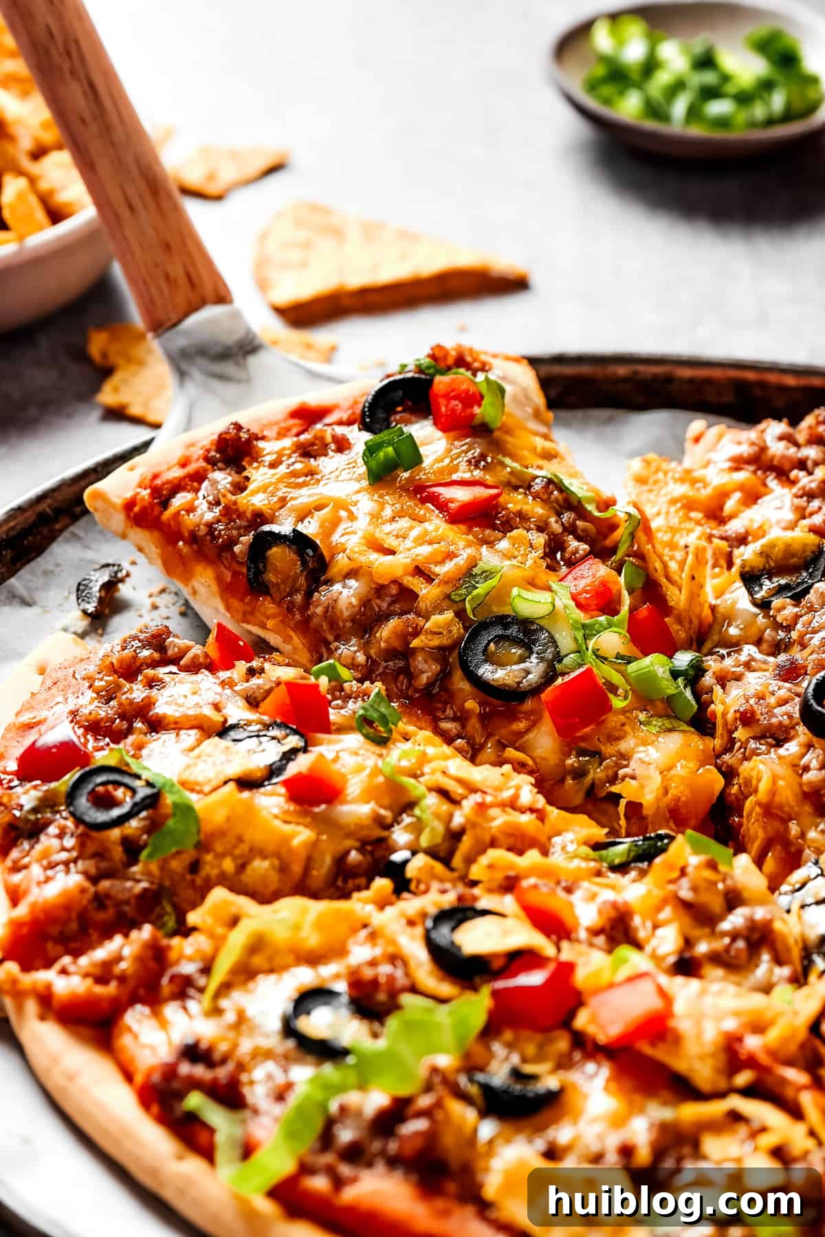 Lifting a perfectly baked slice of taco pizza with a pie server, showcasing its cheesy, topping-laden glory.
